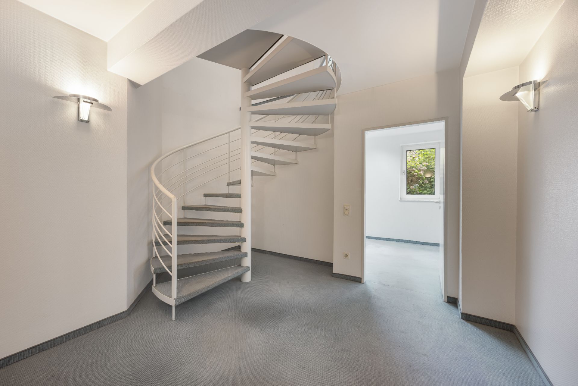Heller Flur mit Wendeltreppe und Blick in einen Raum mit Fenster.