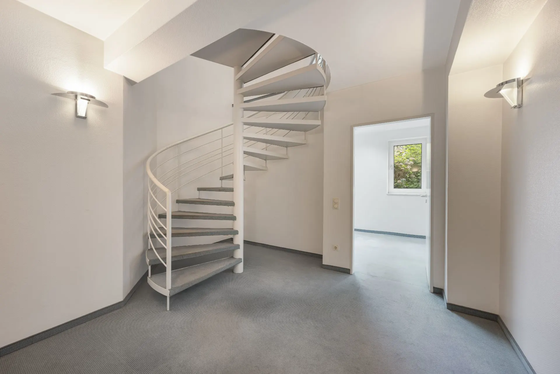 Heller Flur mit Wendeltreppe und Blick in einen Raum mit Fenster.