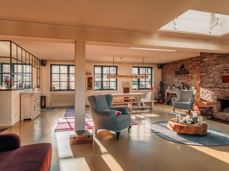 Helles Wohnzimmer mit Sesseln, Esstisch, Kamin und großen Fenstern.