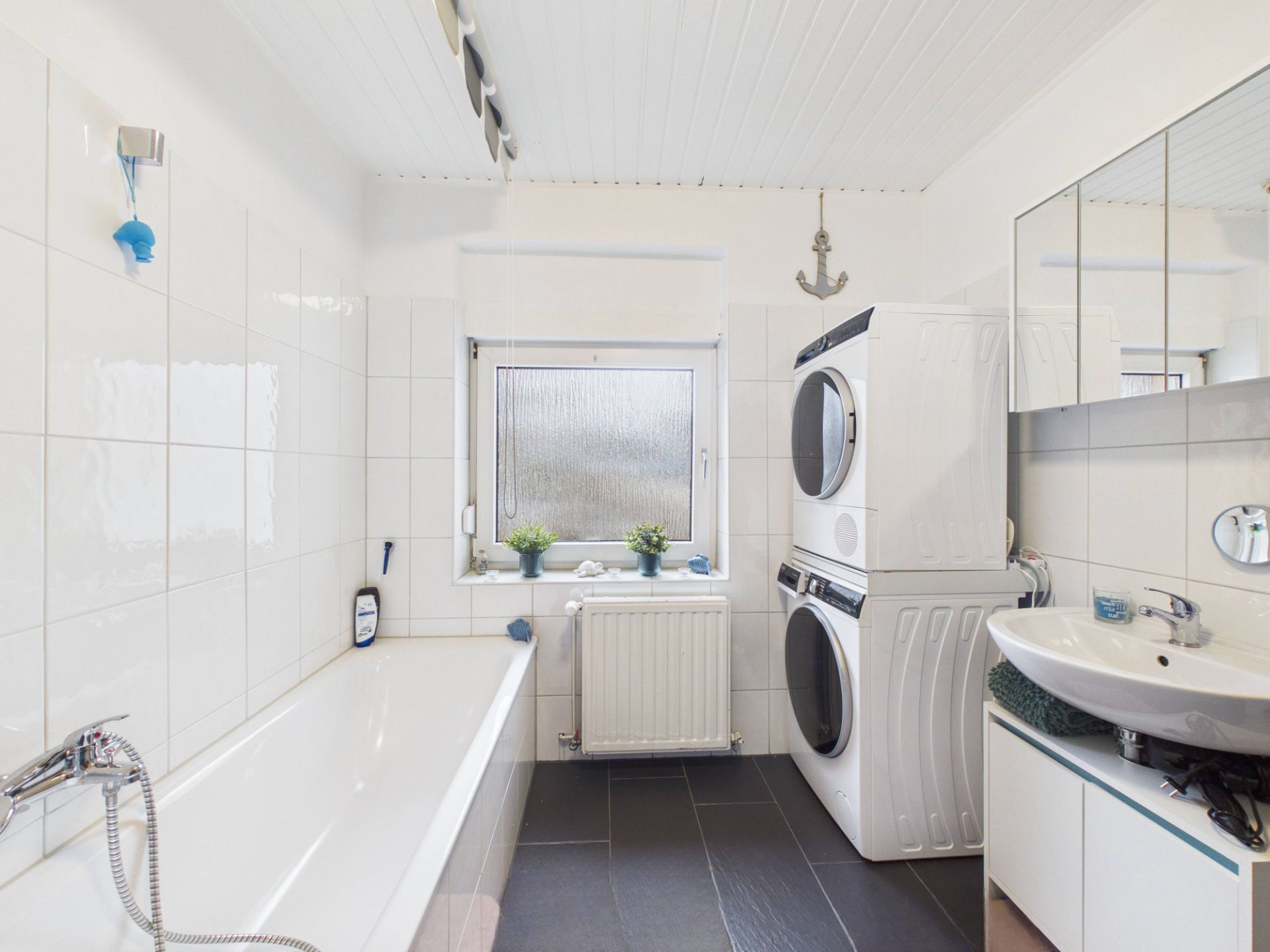 Helles Badezimmer mit Badewanne, Waschbecken, Fenster und gestapelter Waschmaschine und Trockner.