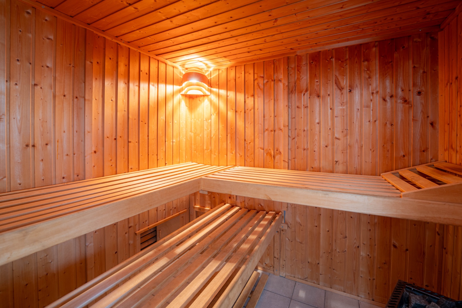 Holzverkleidete Sauna mit zwei Bänken, beleuchtet durch eine Wandlampe.