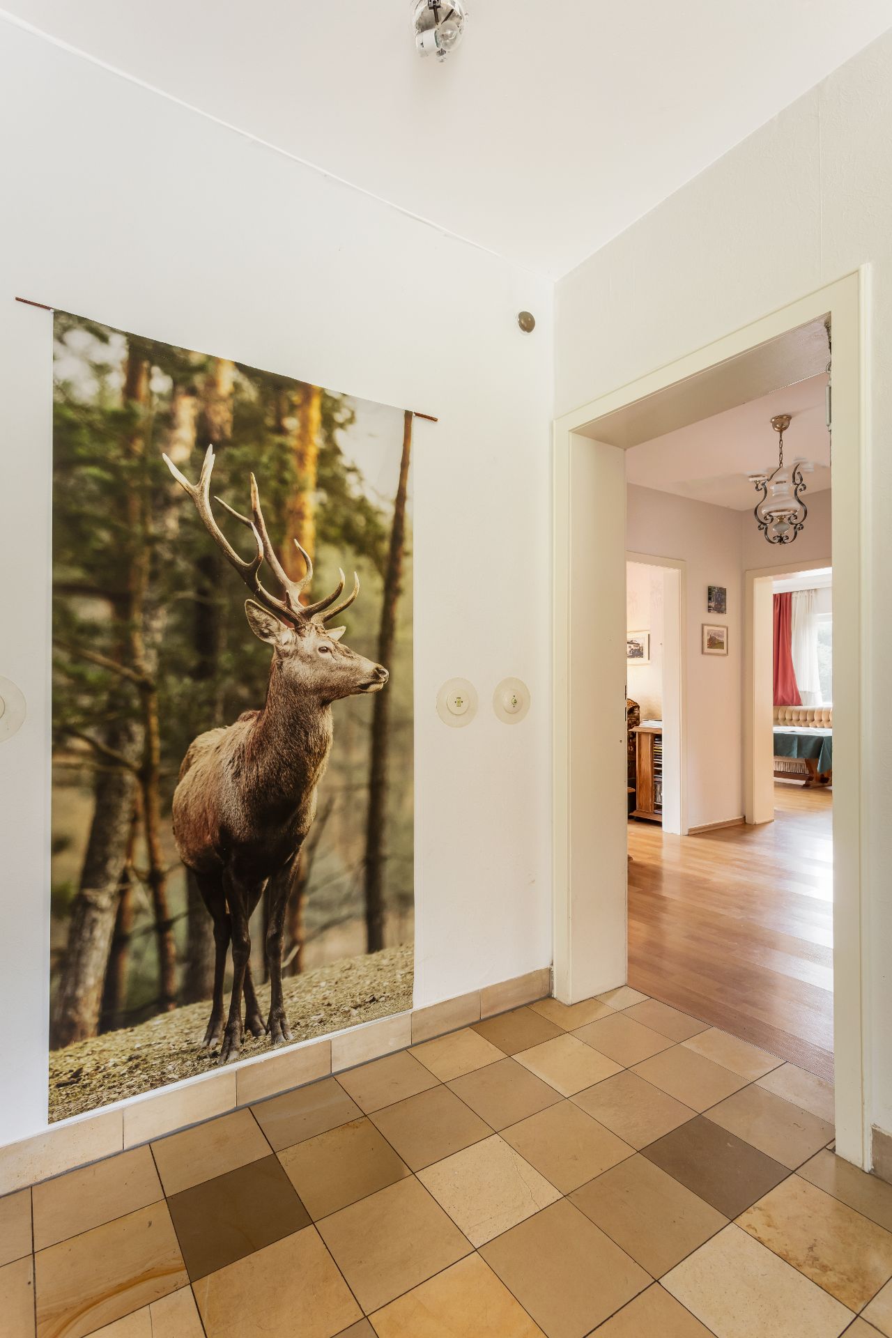 Flur mit Fliesenboden, großem Hirschposter an der Wand und Blick in ein Wohnzimmer.
