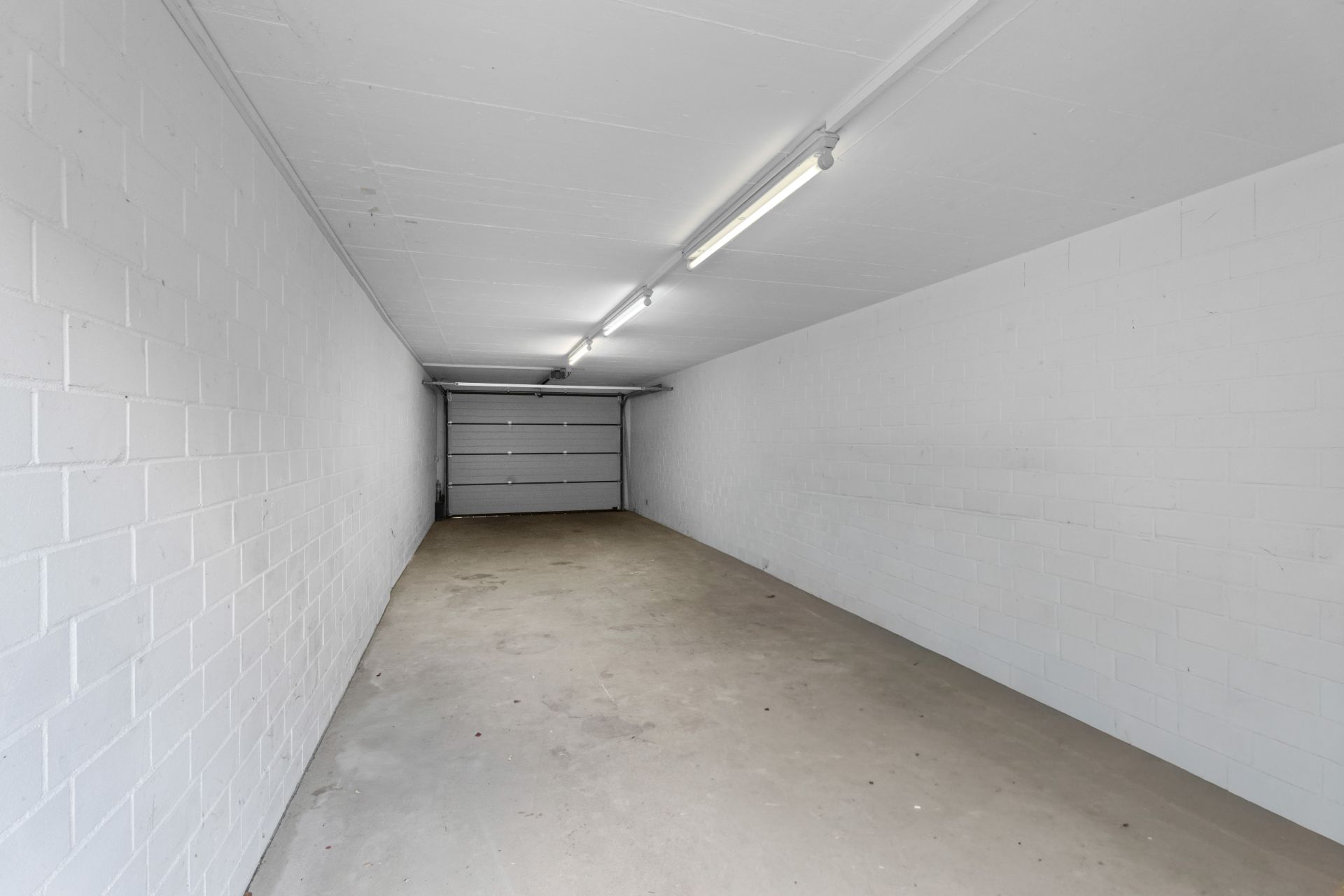 Leere, helle Garage mit geschlossenen Garagentor und weißen Wänden.