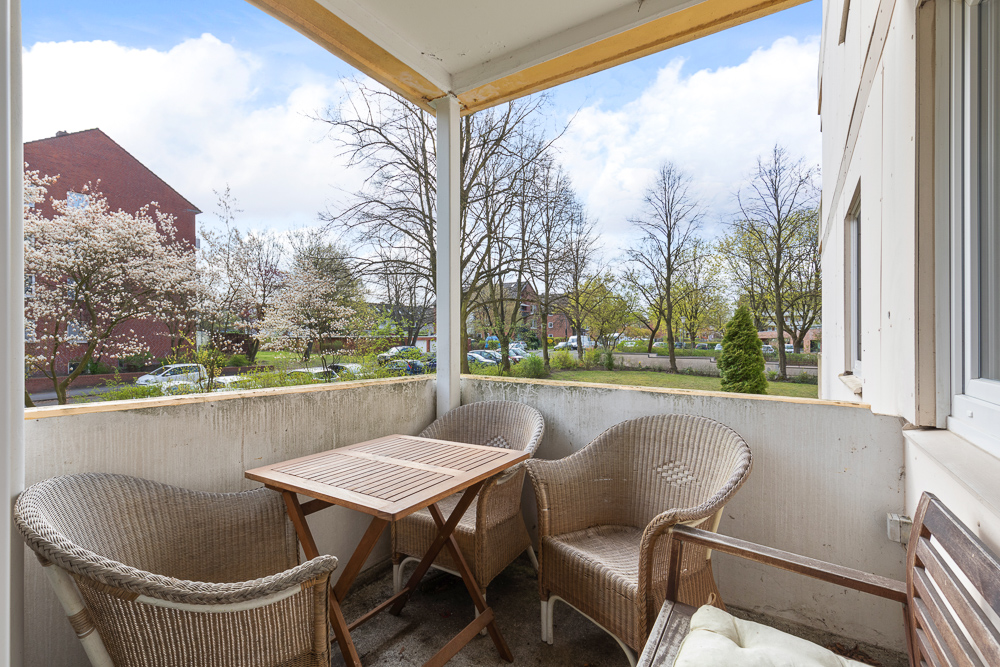 Balkon mit drei Korbstühlen und Holztisch, Blick auf Bäume und Wohnstraße.