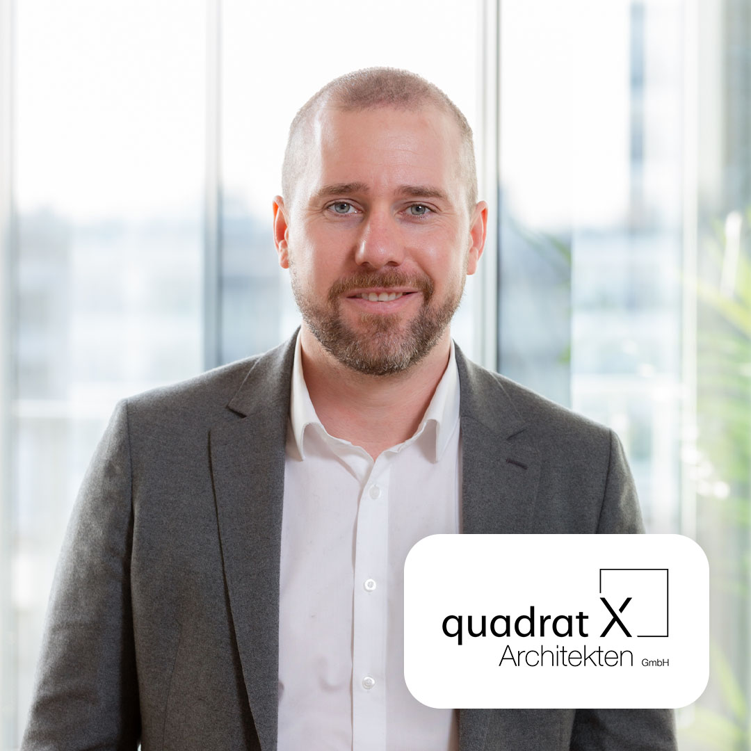 Mann im grauen Anzug steht vor einem großen Fenster. Logo von Quadrat X Architekten ist eingeblendet.