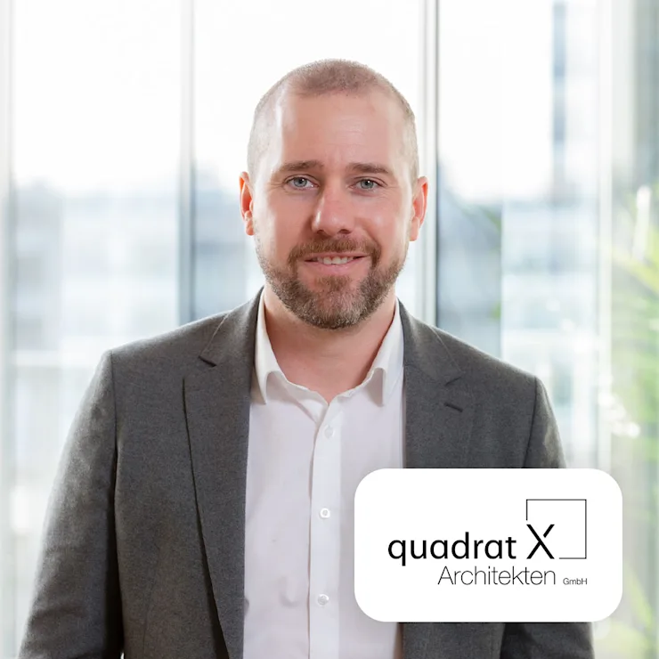 Mann im grauen Anzug steht vor einem großen Fenster. Logo von Quadrat X Architekten ist eingeblendet.