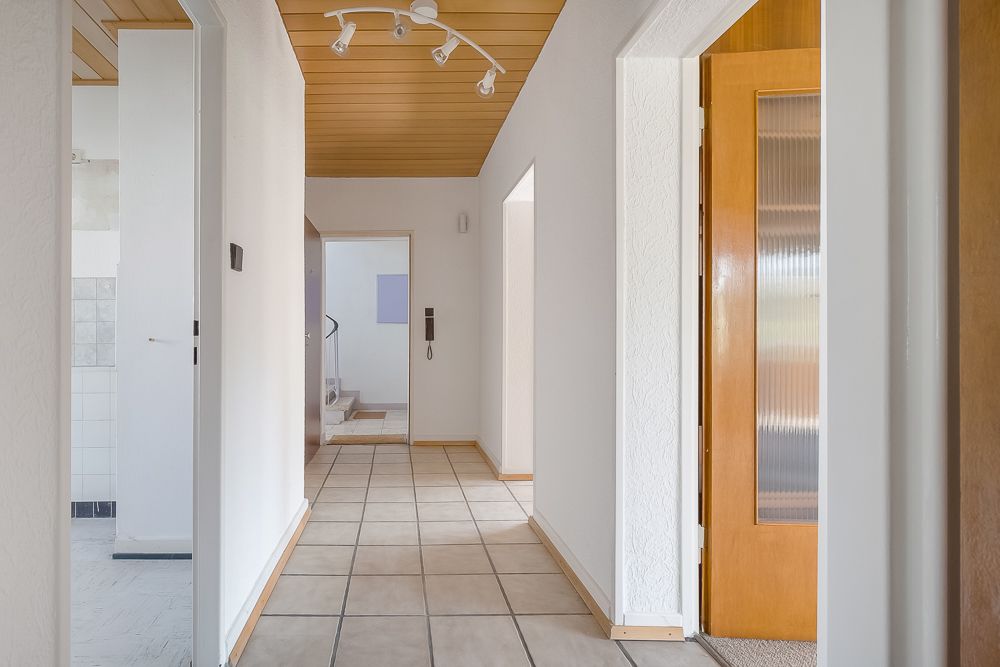 Heller Flur mit Fliesenboden, weißen Wänden und Holztüren in einem Wohnhaus.