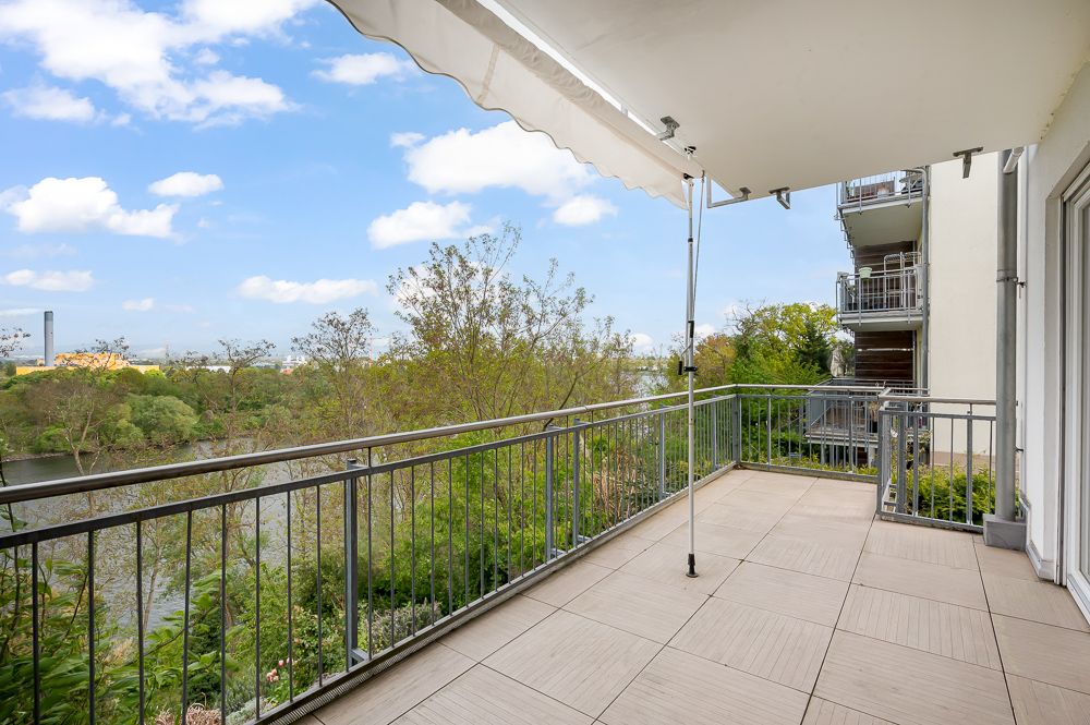 Großer Balkon mit Fliesenboden, Geländer und Blick auf Bäume und einen Fluss.