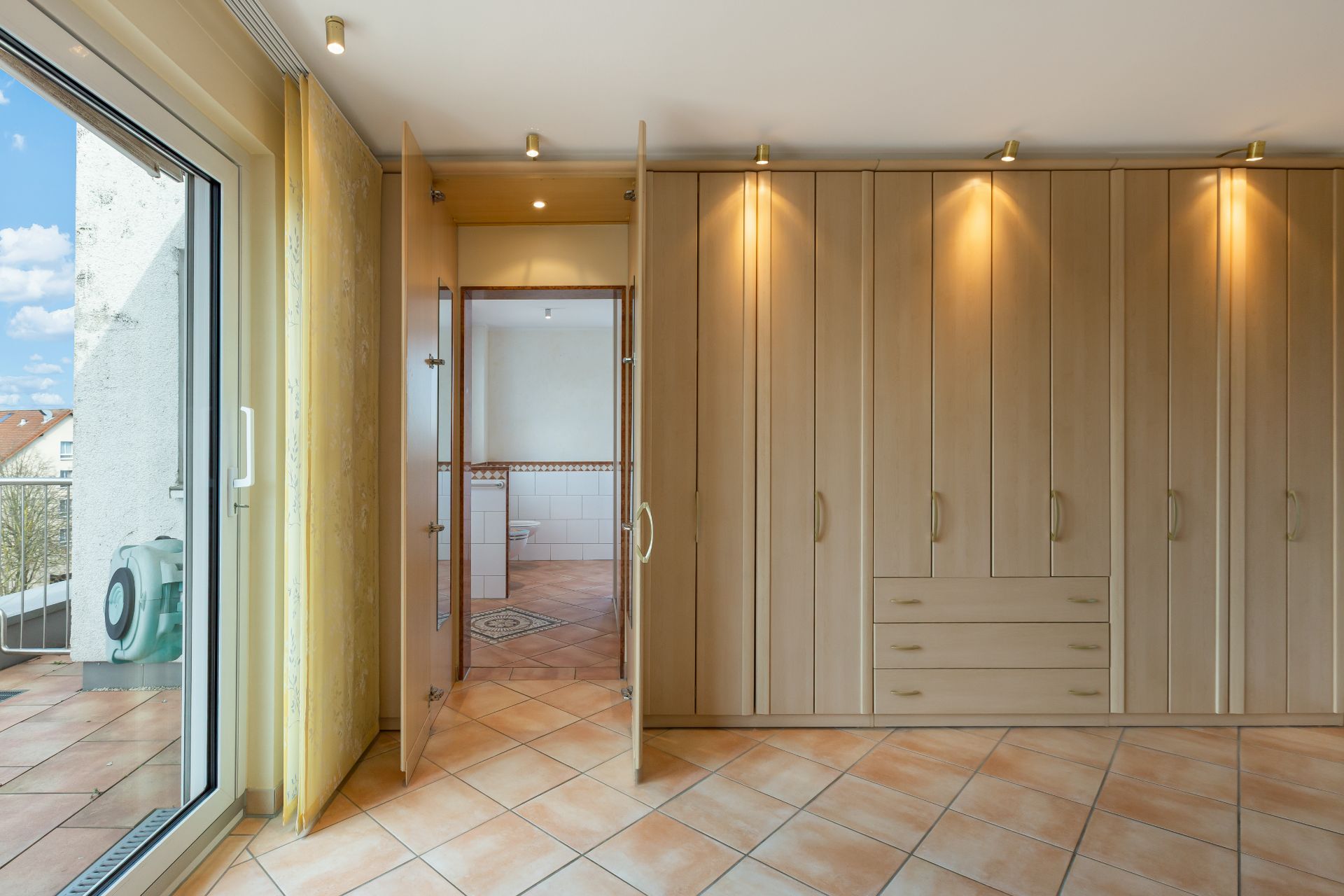Helles Zimmer mit Einbauschrank, Fliesenboden und Zugang zu Balkon und Badezimmer.