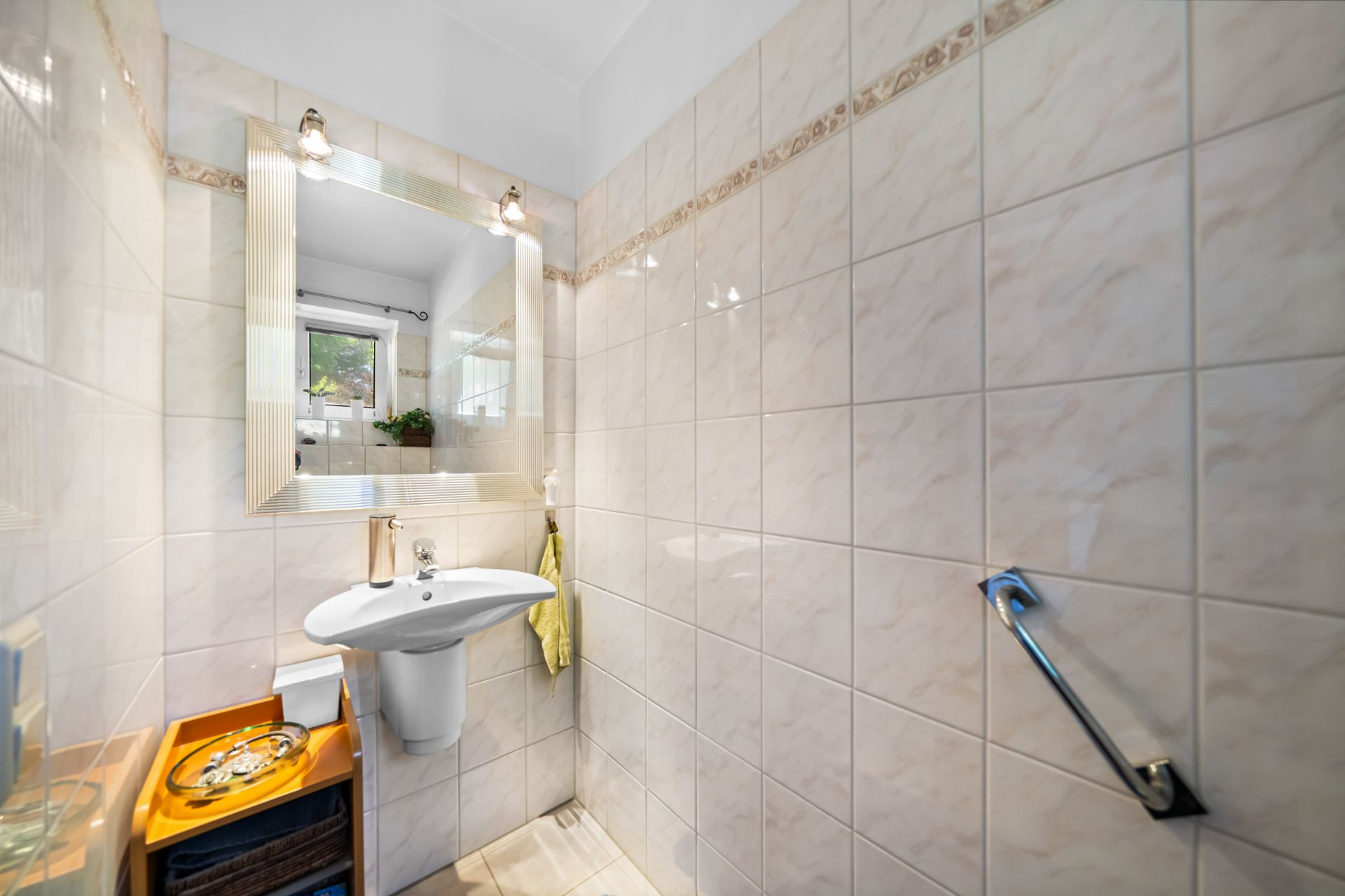 Kleines Badezimmer mit Waschbecken, Spiegel, Handtuch, Fenster und gefliestem Wänden.