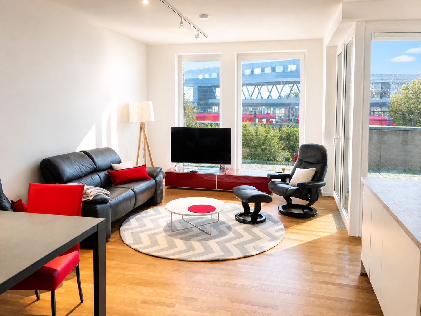 Modernes Wohnzimmer mit Ledersofa, Sessel, Fernseher und großen Fenstern mit Blick nach draußen.