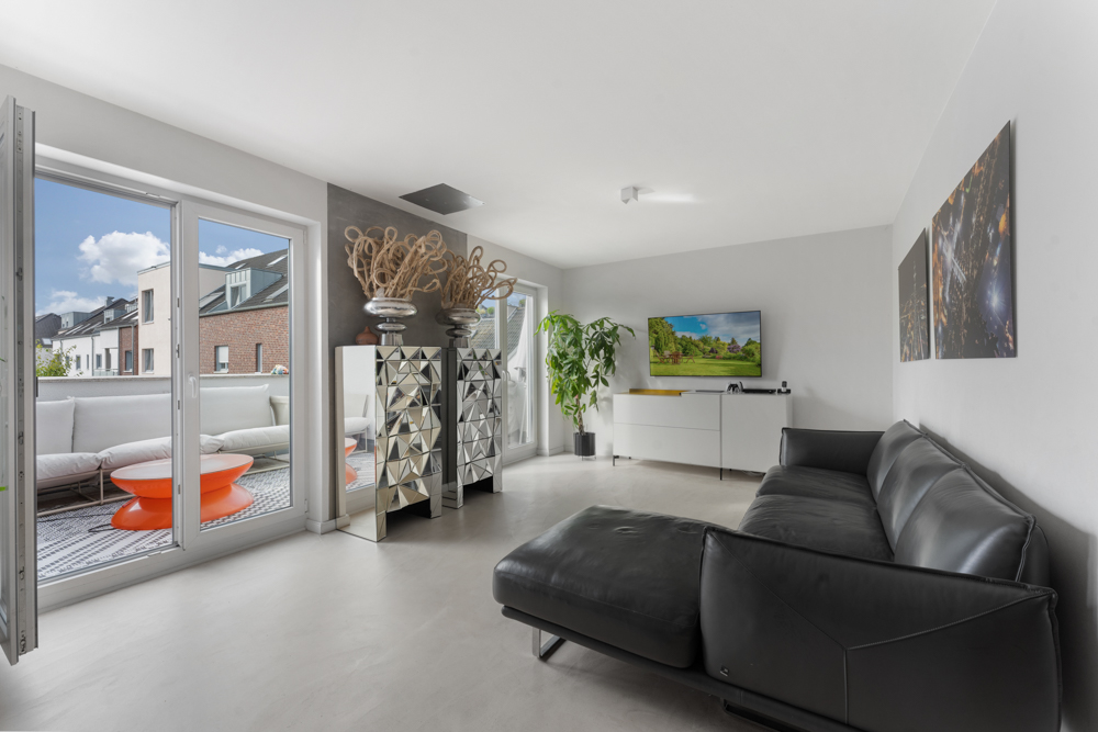 Modernes Wohnzimmer mit schwarzem Sofa, TV, Pflanze und Zugang zu einem Balkon.