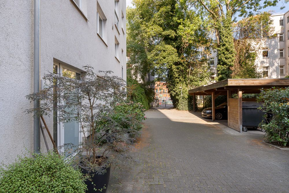 Gepflasterter Hof mit überdachtem Carport, Pflanzen und angrenzendem Wohngebäude.