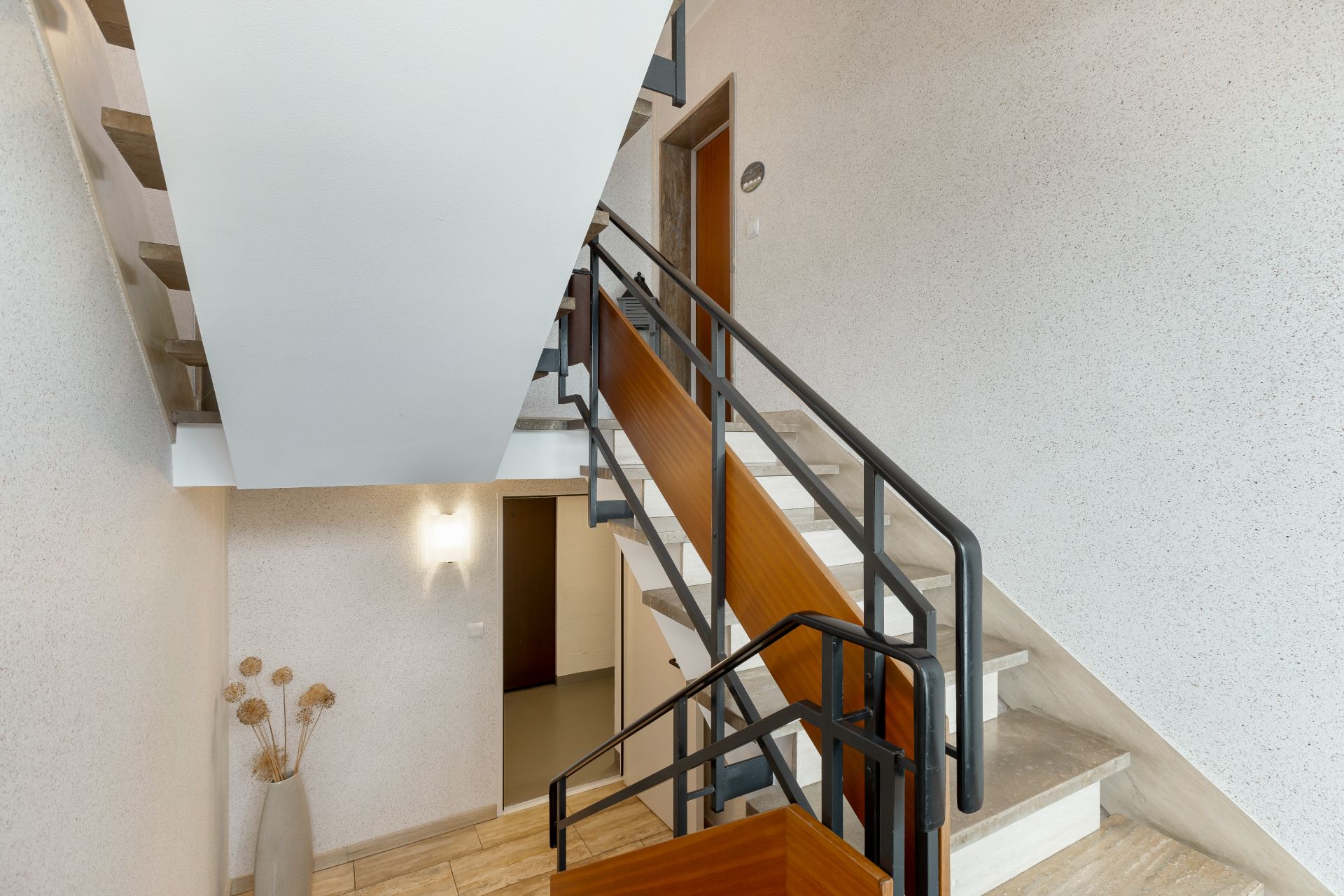 Innenansicht eines Treppenhauses mit Holzgeländer und Dekovase mit Trockenblumen.