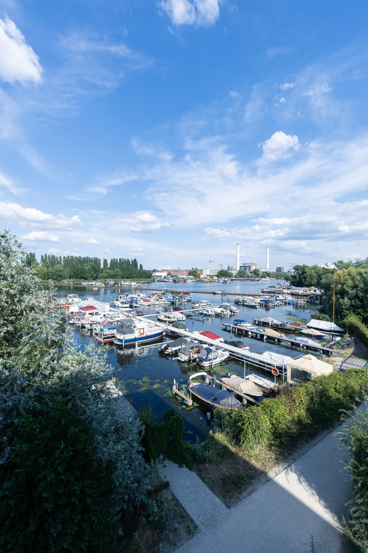 Blick auf einen kleinen Hafen mit mehreren Booten und Stegen, umgeben von Bäumen und Gehwegen.