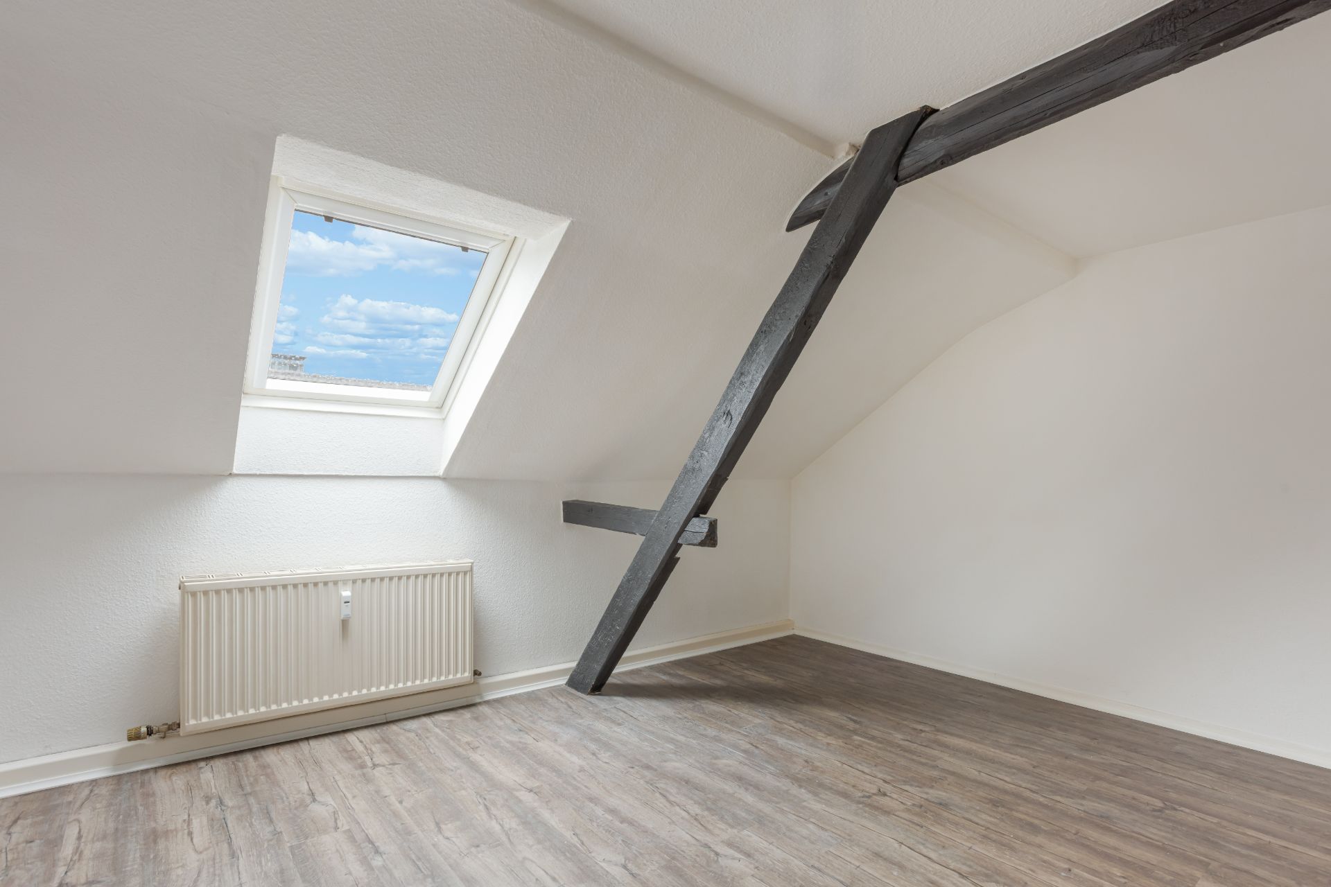 Heller Dachraum mit Fenster, sichtbarem Balken, Heizkörper und Laminatboden.