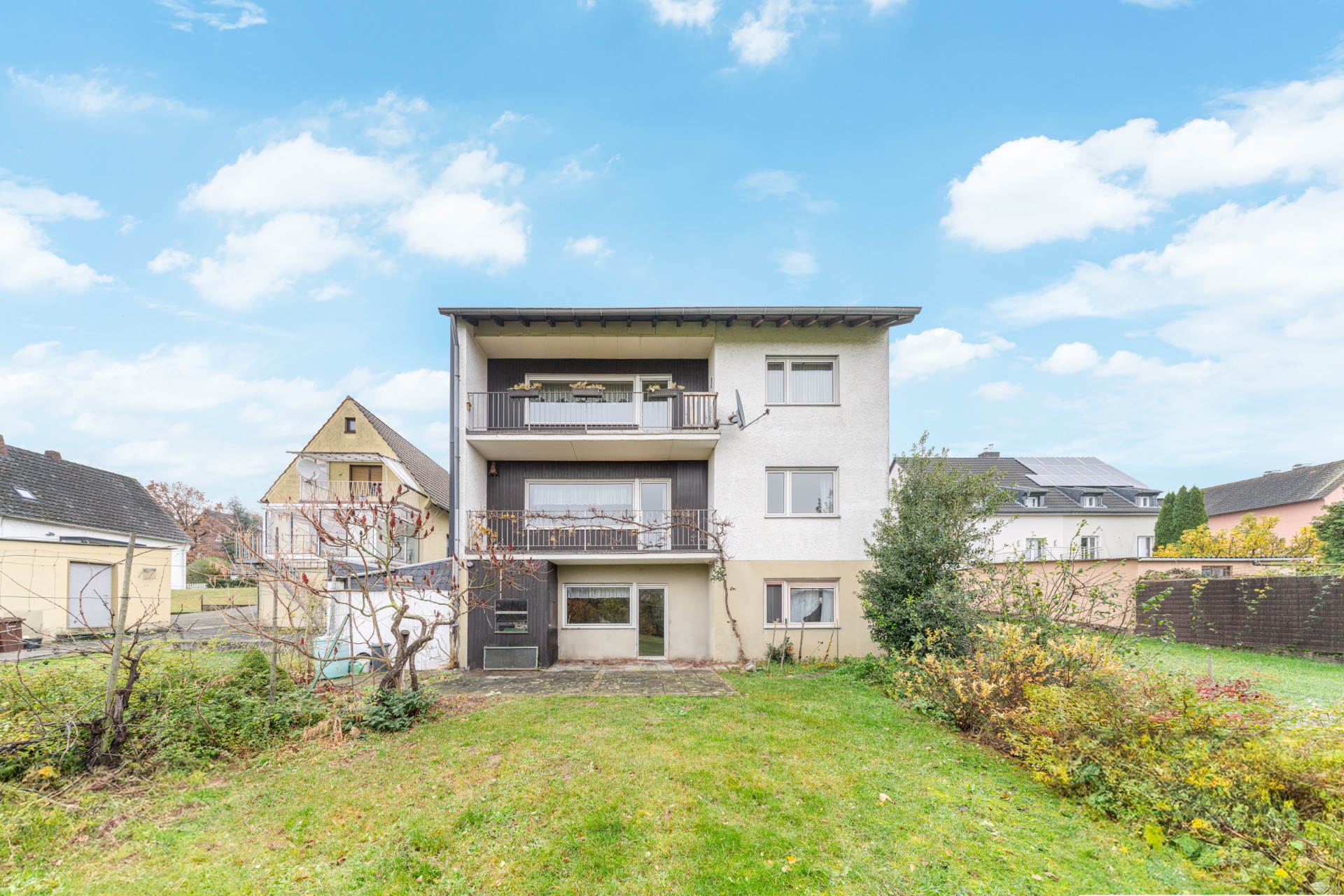 Dreistöckiges Wohnhaus mit zwei Balkonen und Garten im Vordergrund.