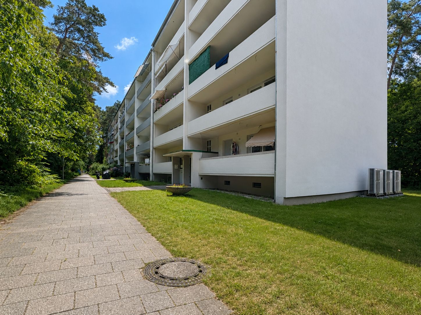 Mehrstöckiges Wohnhaus mit Balkonen, Grünfläche und Gehweg im Vordergrund.