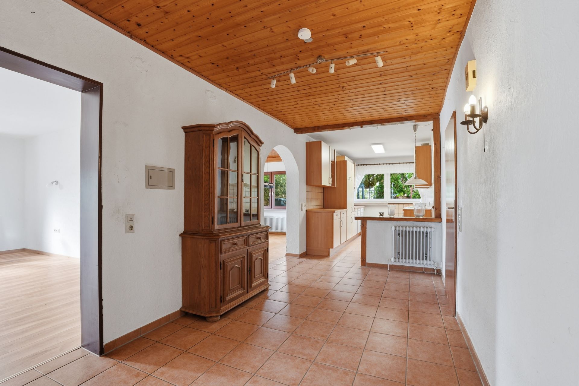 Flur mit Holzdecke, Fliesenboden, Schrank und Blick in eine helle Küche mit Fenster.