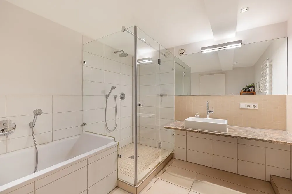 Modernes Badezimmer mit Badewanne, Glasdusche und breitem Waschtisch mit Spiegel.