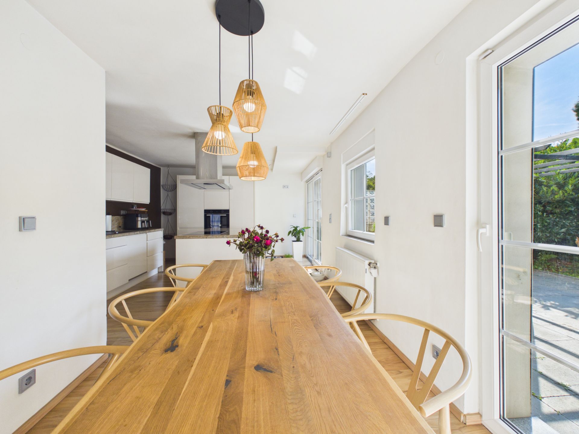 Heller Essbereich mit Holztisch, Holzstühlen und Hängelampen, Blick in moderne Küche.