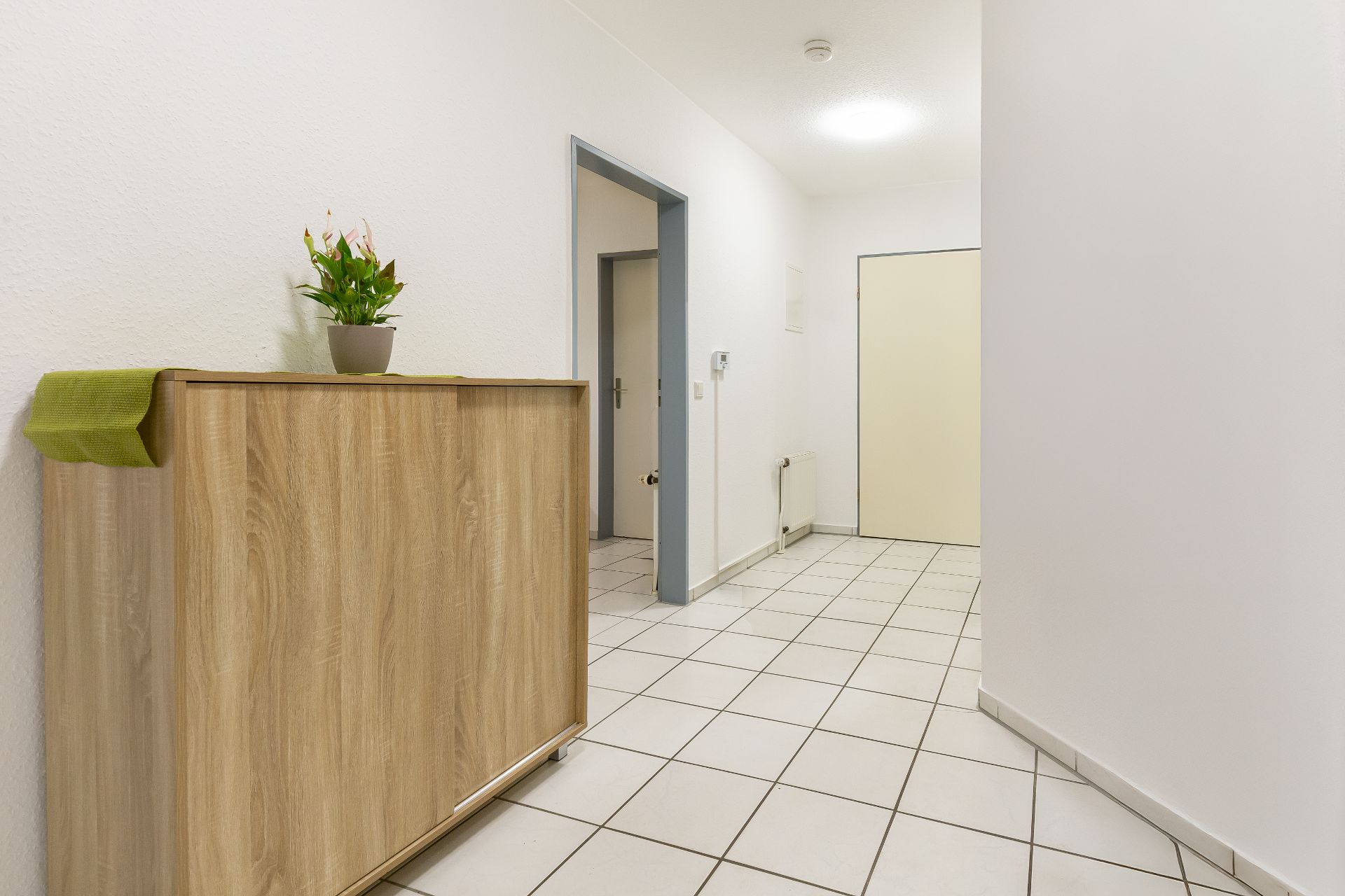 Heller Flur mit Fliesenboden, Holzkommode und Topfpflanze auf der Kommode.