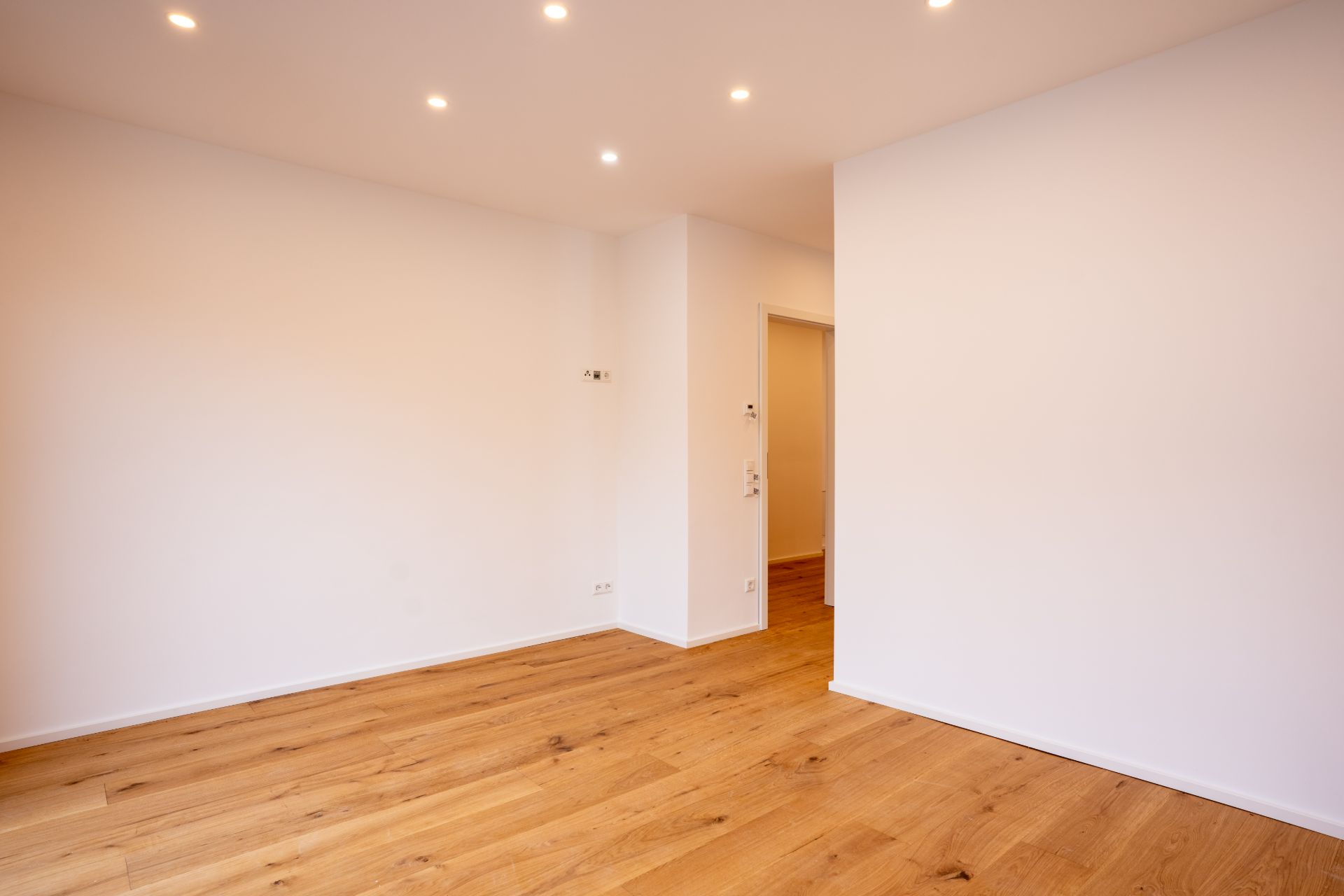 Heller Raum mit Holzfußboden und weißen Wänden, Deckenstrahler an der Decke.