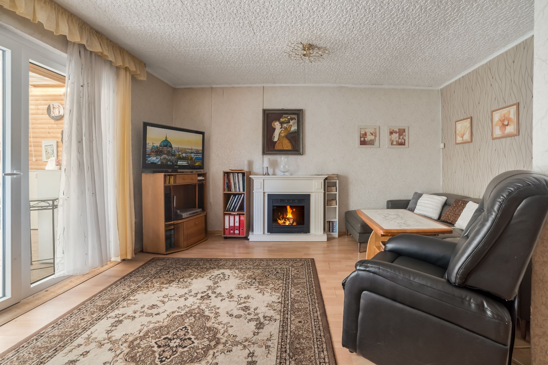 Wohnzimmer mit Kamin, Sofa, Sessel, Teppich, Fernseher und Bildern an der Wand.