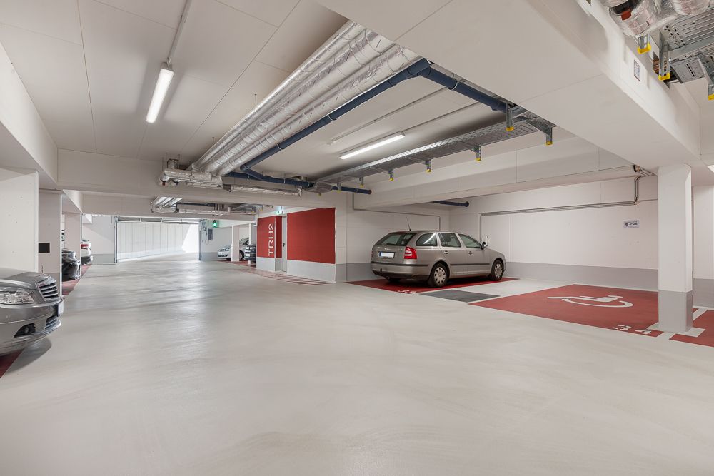 Helle Tiefgarage mit mehreren geparkten Autos und markierten Parkplätzen, darunter ein Behindertenparkplatz.