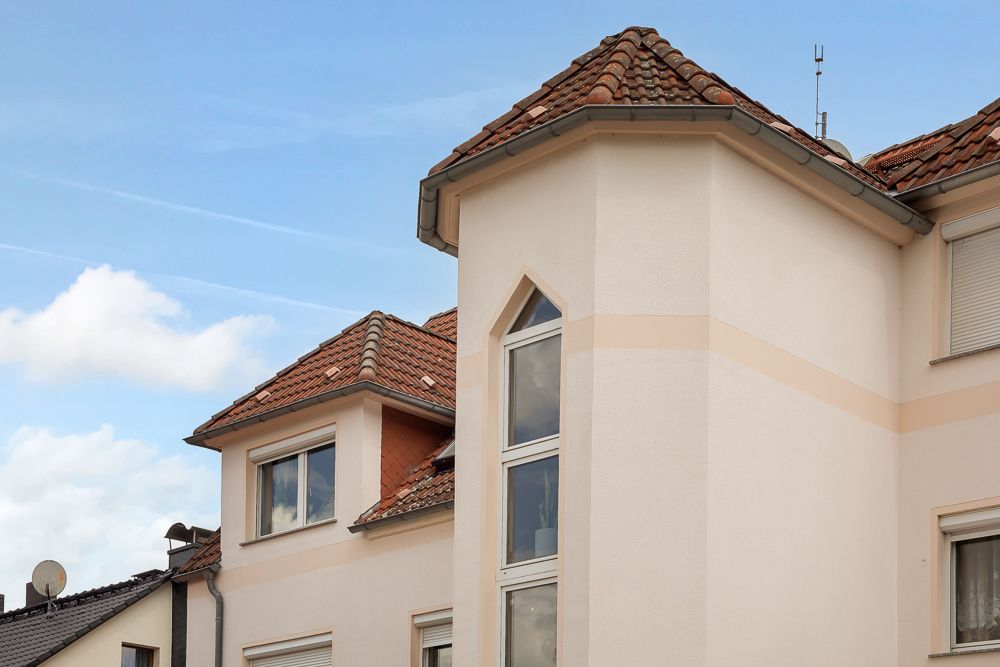 Fassade eines Wohnhauses mit Erker und roten Dachziegeln unter blauem Himmel.