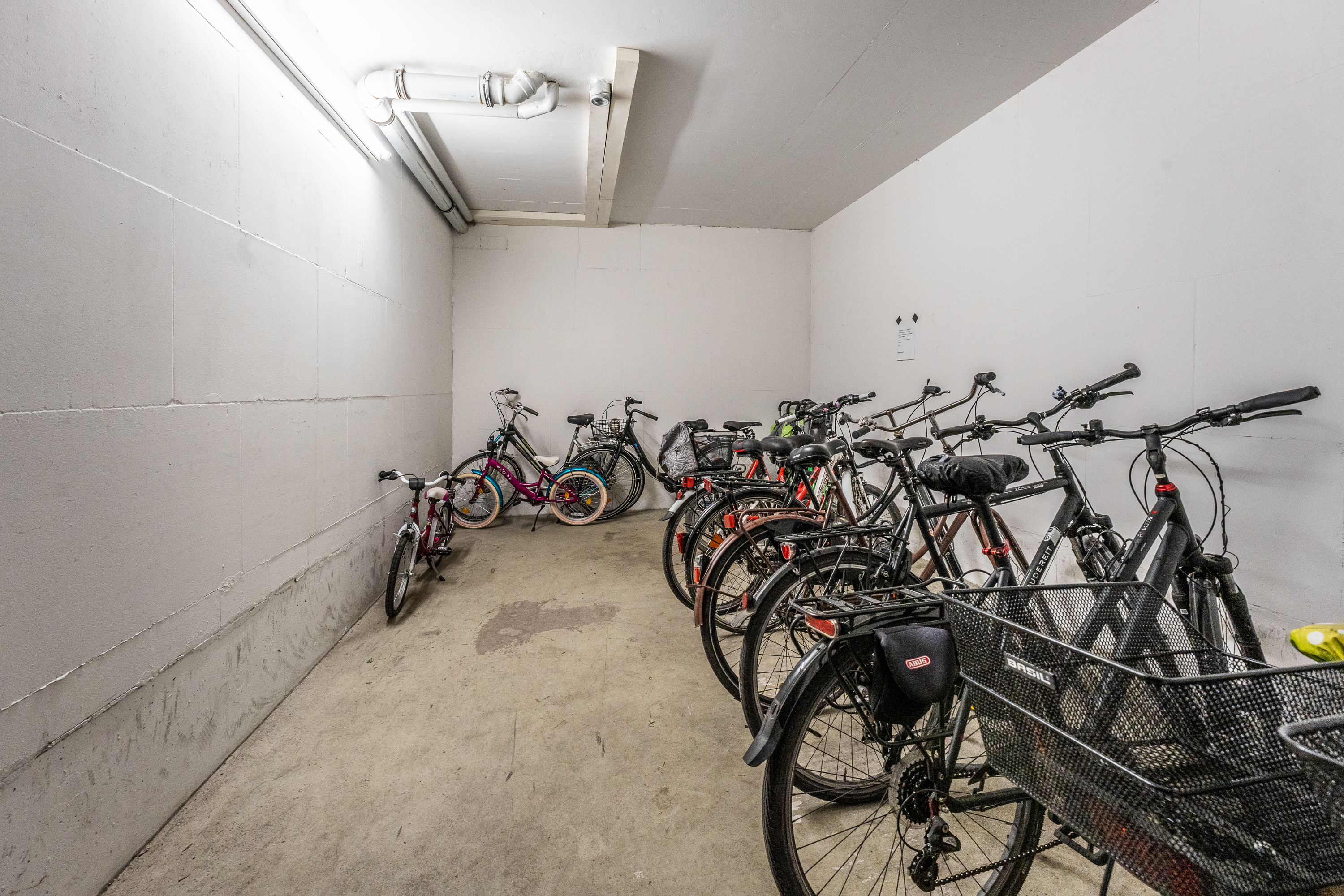 Fahrradkeller mit mehreren abgestellten Fahrrädern in einem weißen Raum.