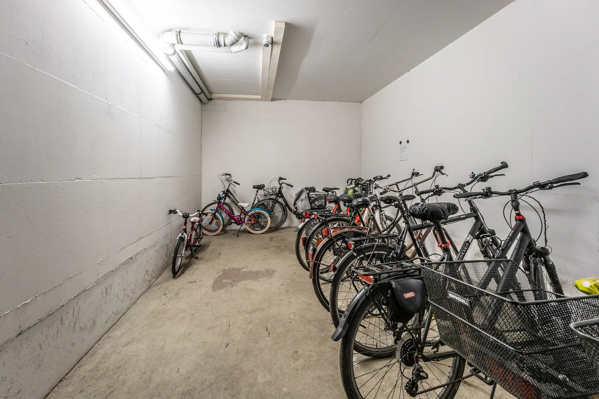 Fahrradkeller mit mehreren abgestellten Fahrrädern in einem weißen Raum.