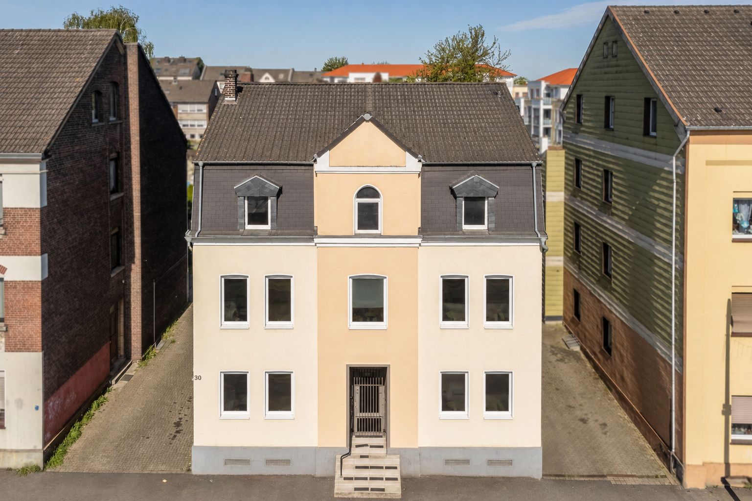 Vorderansicht eines dreistöckigen Wohnhauses mit hellem Anstrich und sechs Fenstern.