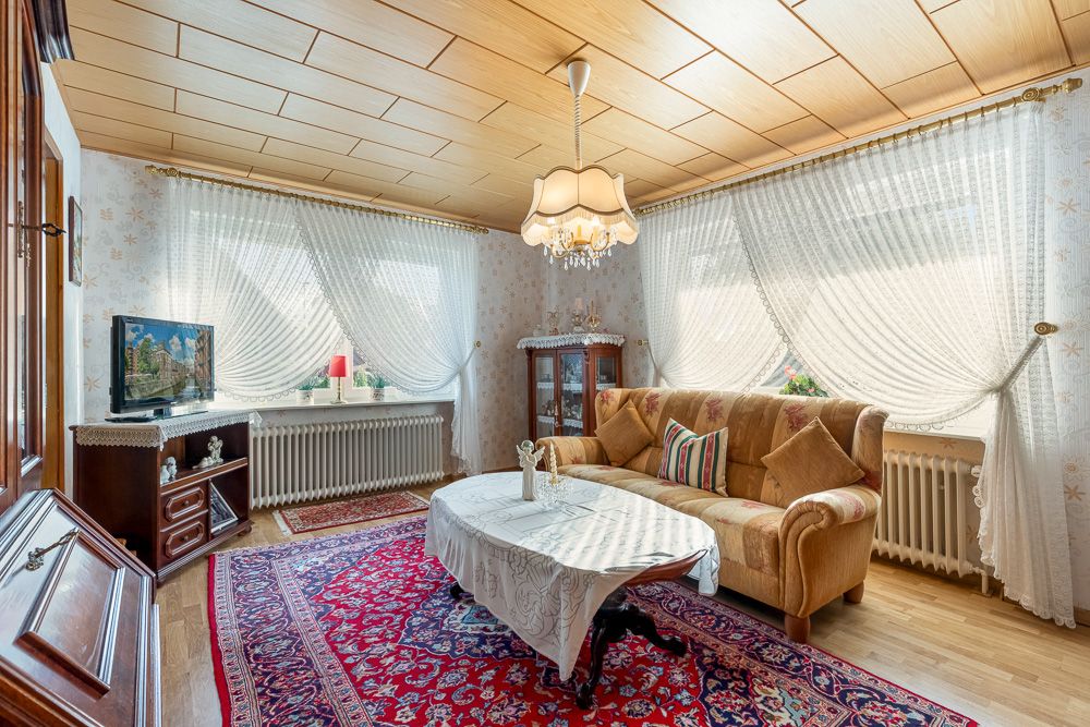 Helles Wohnzimmer mit Sofa, Couchtisch, Teppich und großem Fenster mit weißen Gardinen.