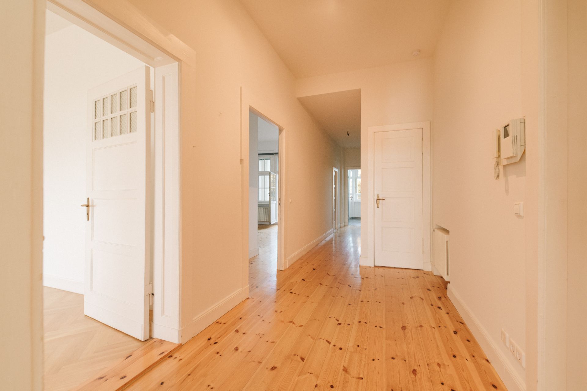 Heller Flur mit Holzboden, weißen Türen und Wänden, mehrere Zimmer sind sichtbar.