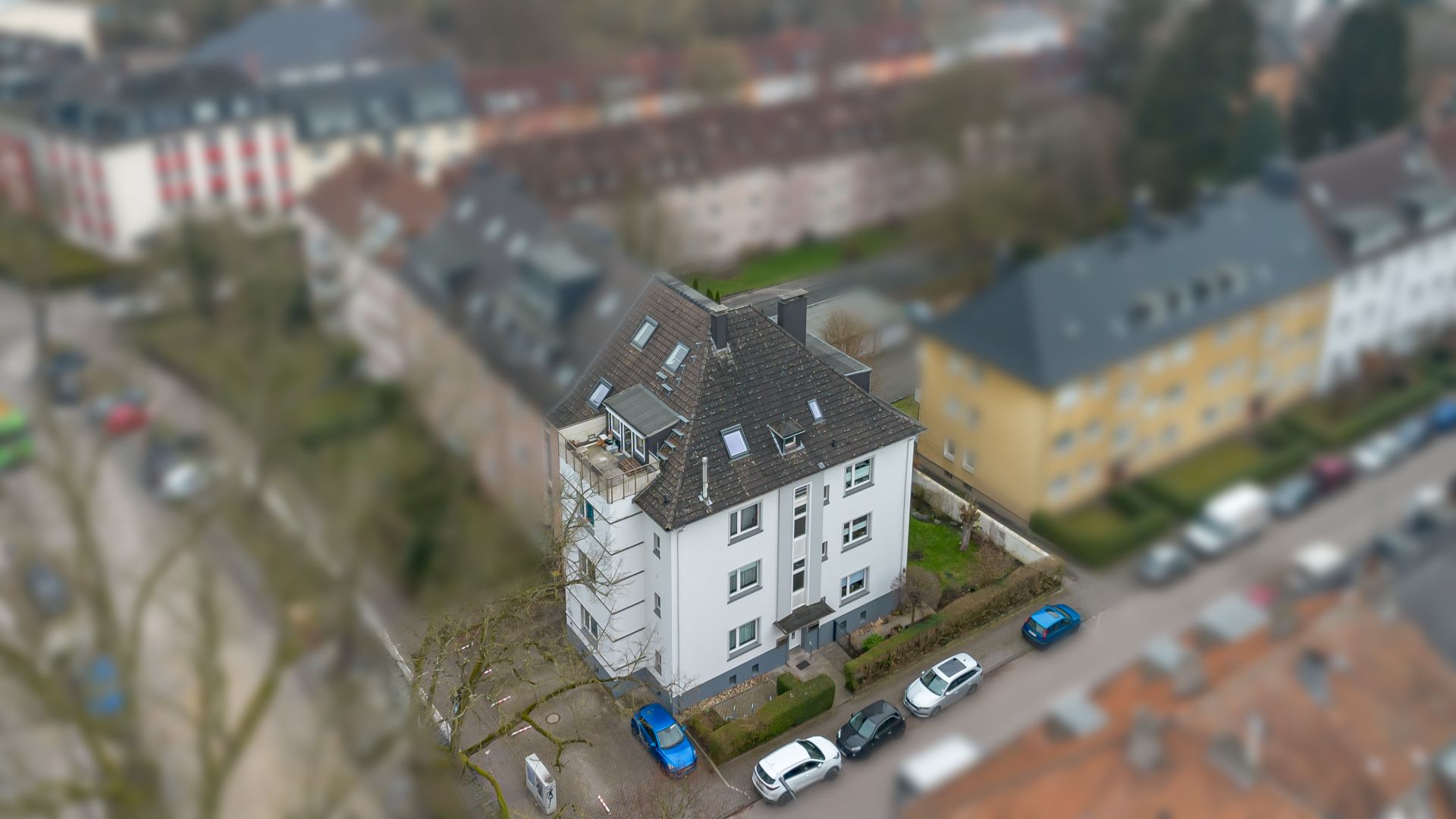 Mehrfamilienhaus mit Balkon und Autos davor auf einer Wohnstraße.