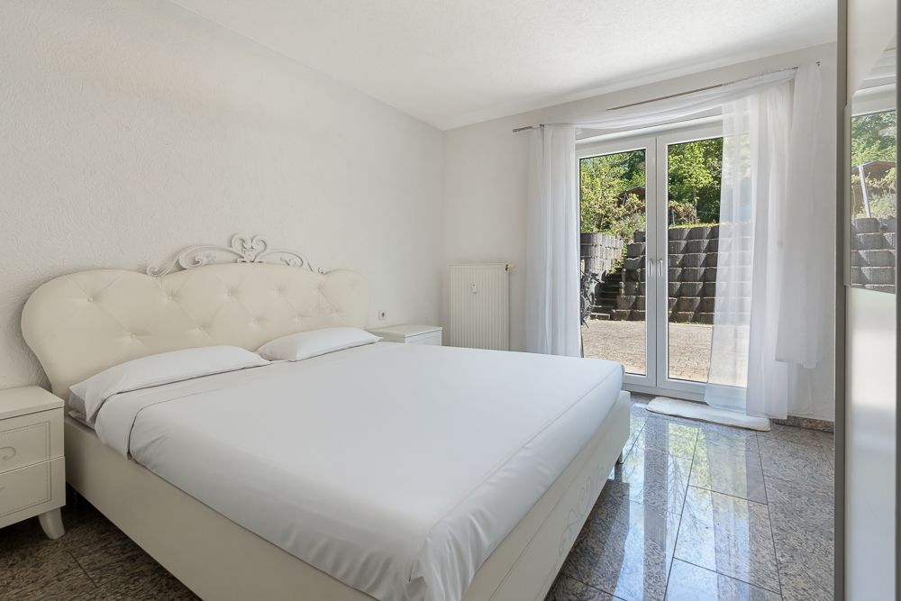 Helles Schlafzimmer mit Doppelbett, Nachttischen und Glastür zur Terrasse.