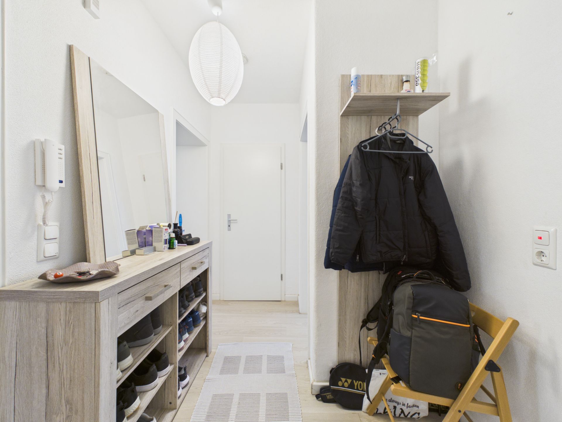 Flur mit Schuhregal, Spiegel, Garderobe und Jacken an der Wand.