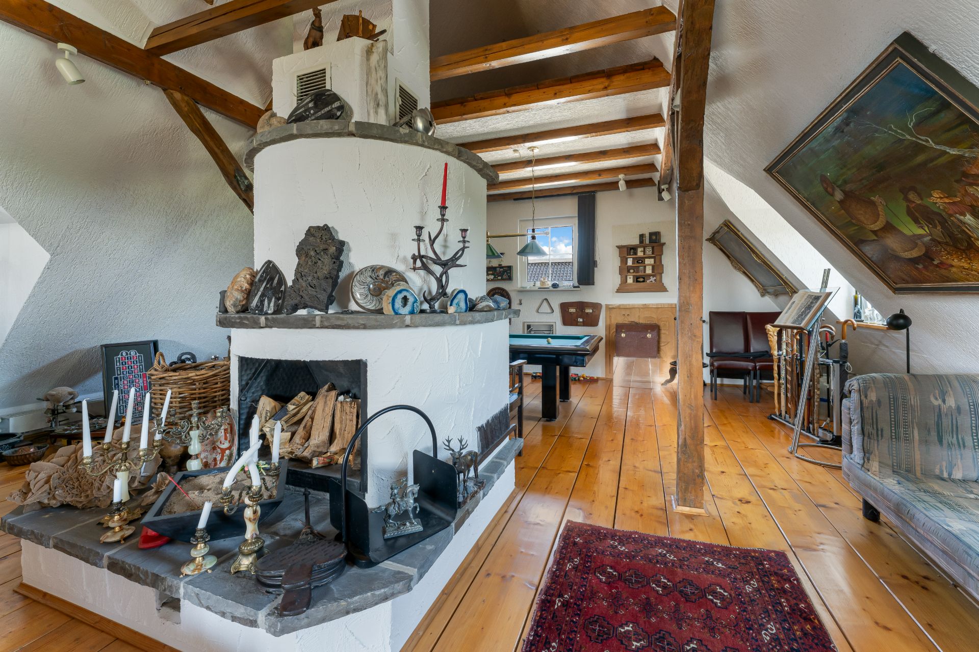 Wohnzimmer mit Kamin, Holzboden, sichtbaren Deckenbalken und Dekorationsgegenständen.