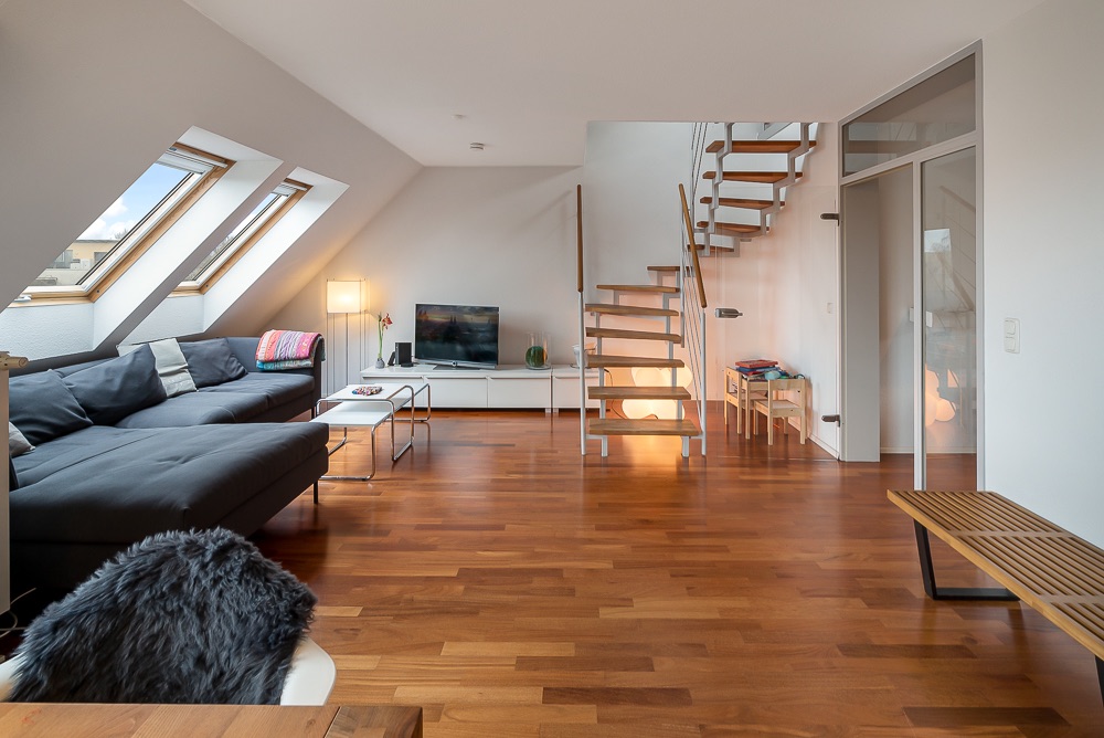 Modernes Wohnzimmer mit Holzfußboden, Sofa, Fernseher und offener Treppe.