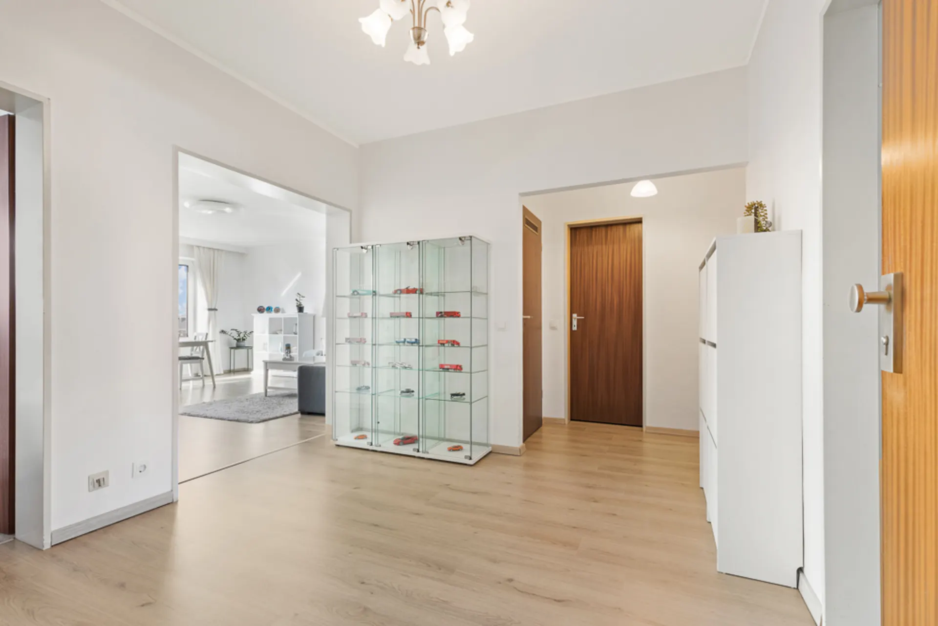 Heller Flur mit Holzfußboden, Vitrine mit Modellautos und Blick ins Wohnzimmer.