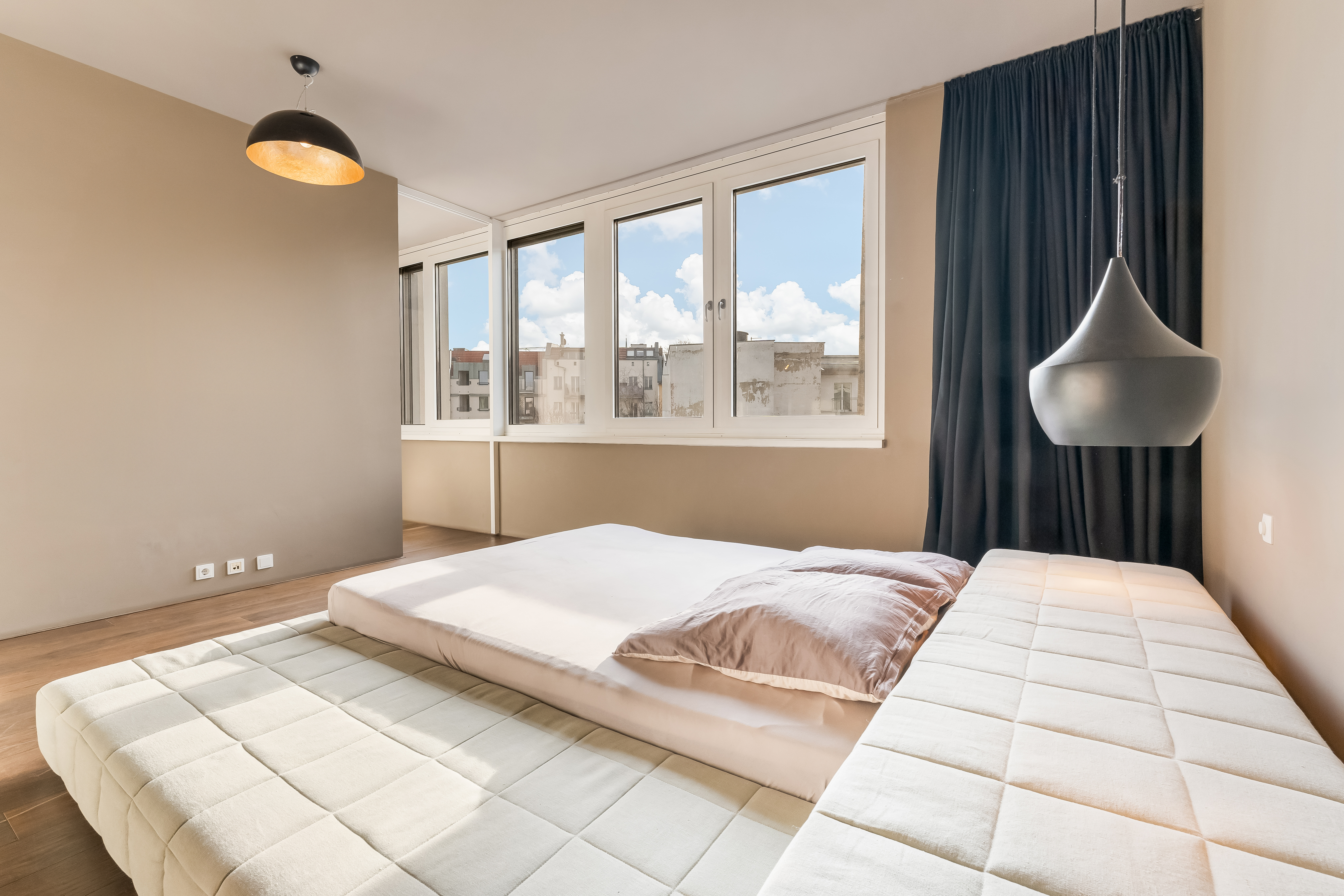 Helles Schlafzimmer mit großem Bett, Fenstern und modernen Hängelampen.