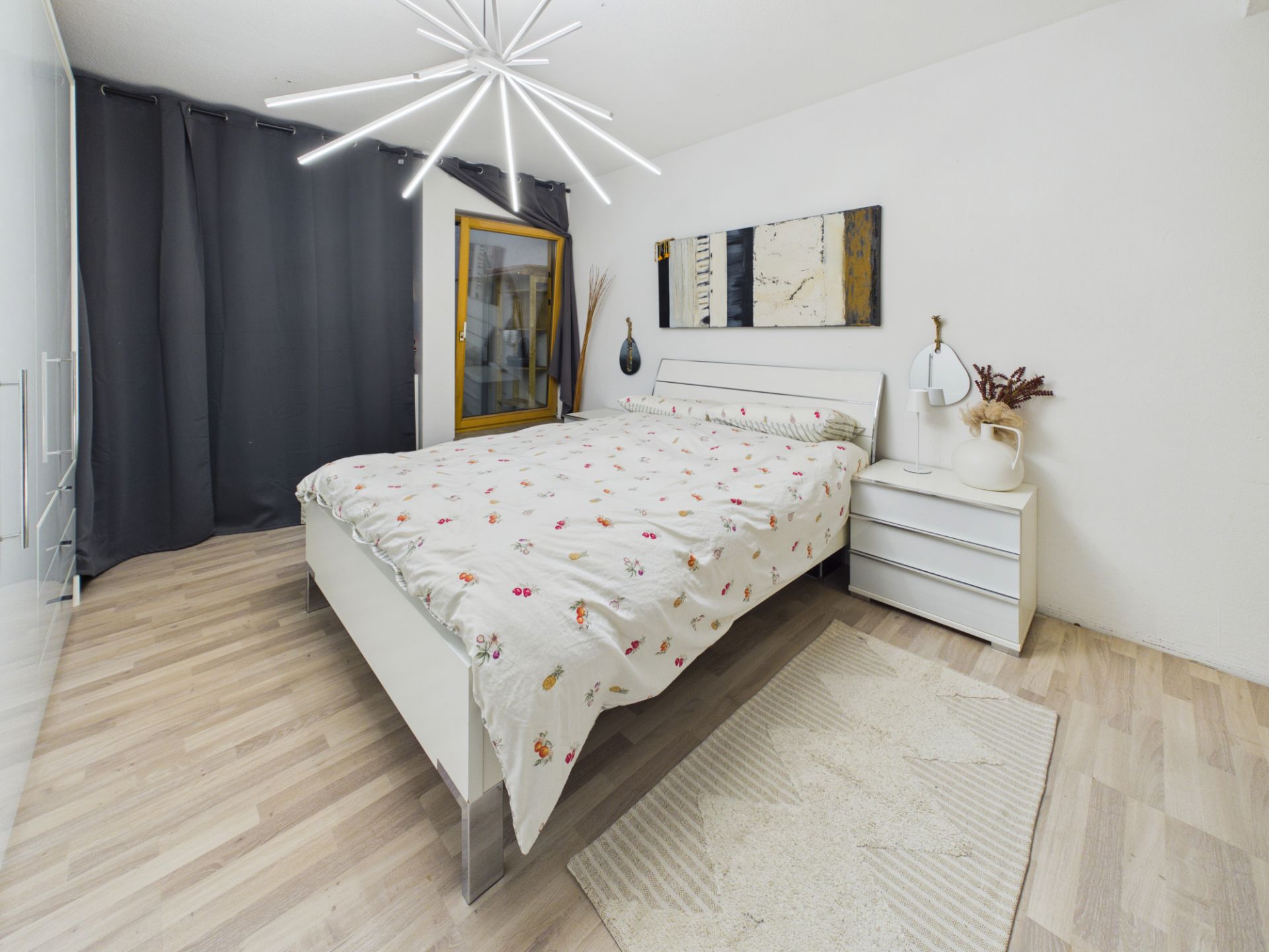 Helles Schlafzimmer mit Doppelbett, Nachttisch, Kunst an der Wand und modernem Kronleuchter.