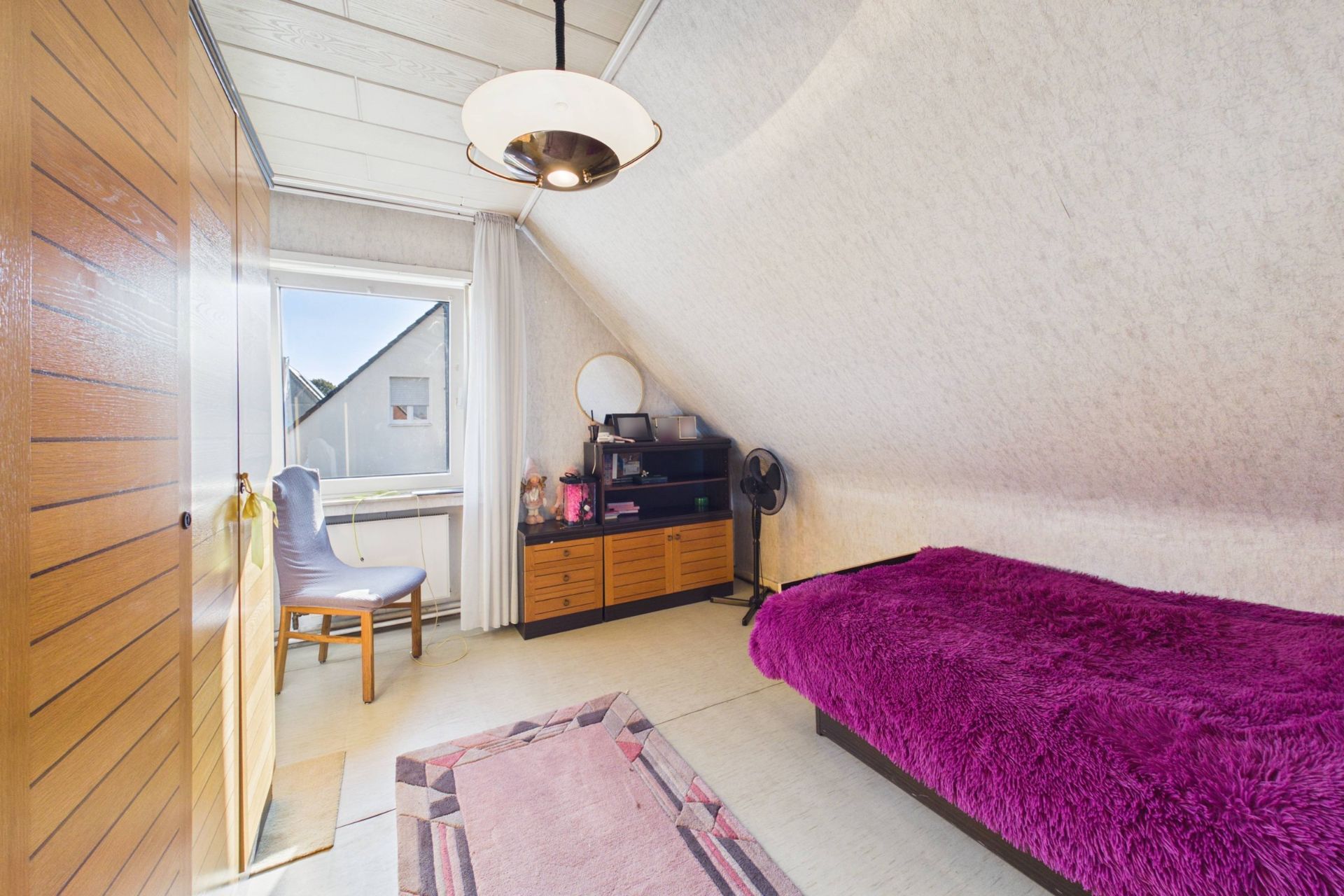 Kleines Schlafzimmer mit Einzelbett, lila Decke, Teppich, Schrank und Fenster.