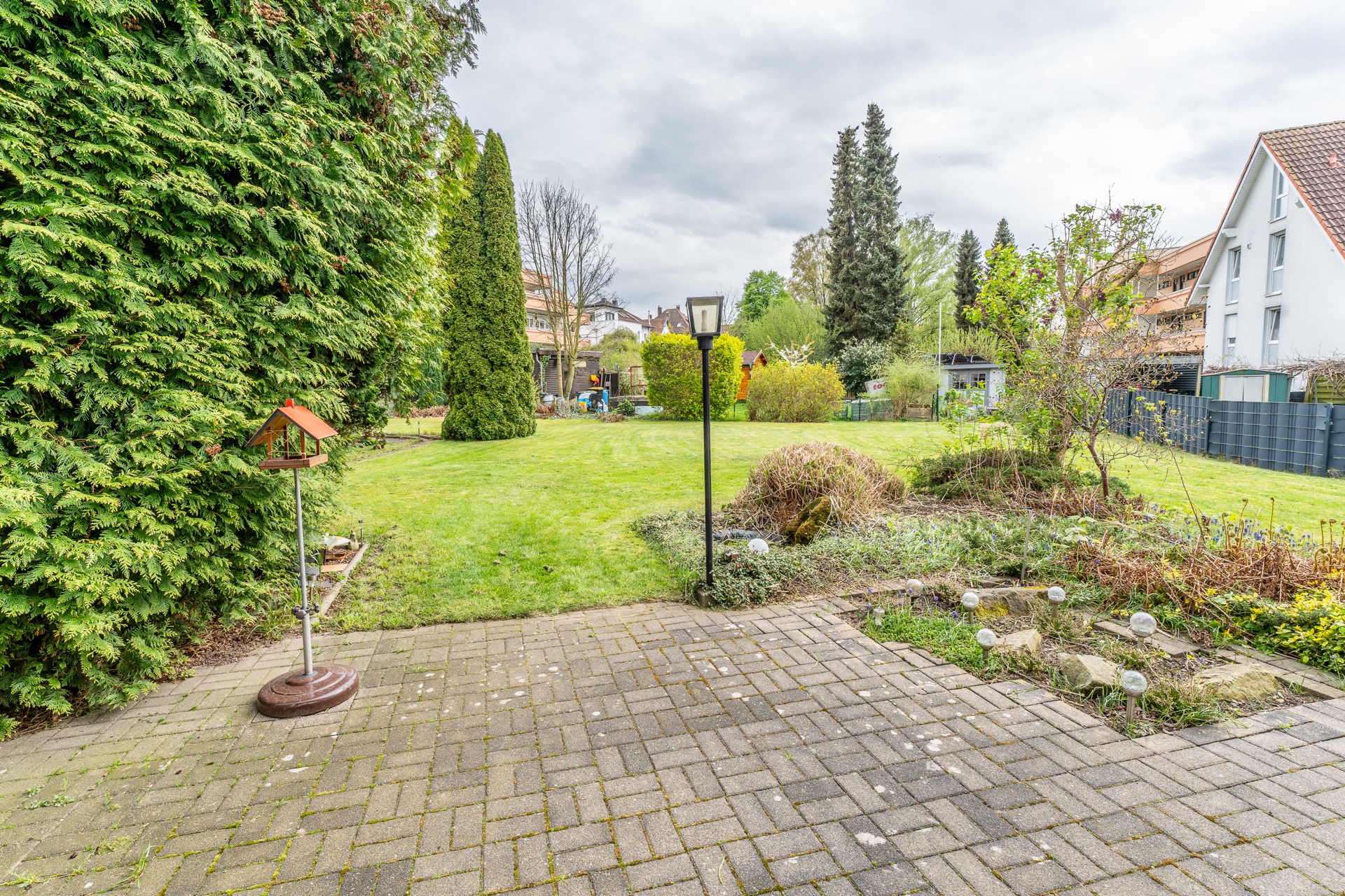Gepflasterte Terrasse mit Blick auf großen grünen Garten, Sträucher und Bäume.