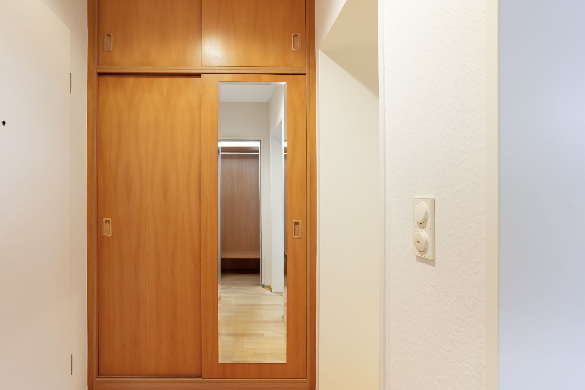 Holzschrank mit Schiebetüren und einem Spiegel in einem Flur.