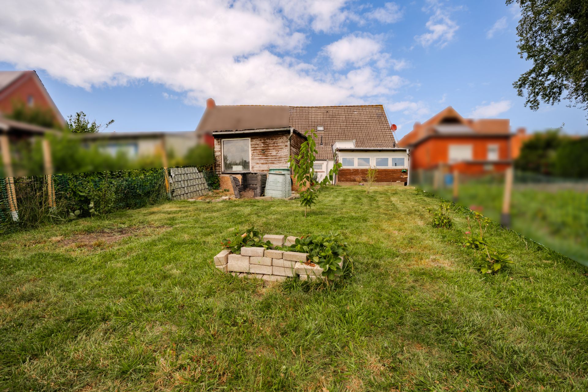Garten mit Rasenfläche, Steinbeet und kleinem Haus im Hintergrund.