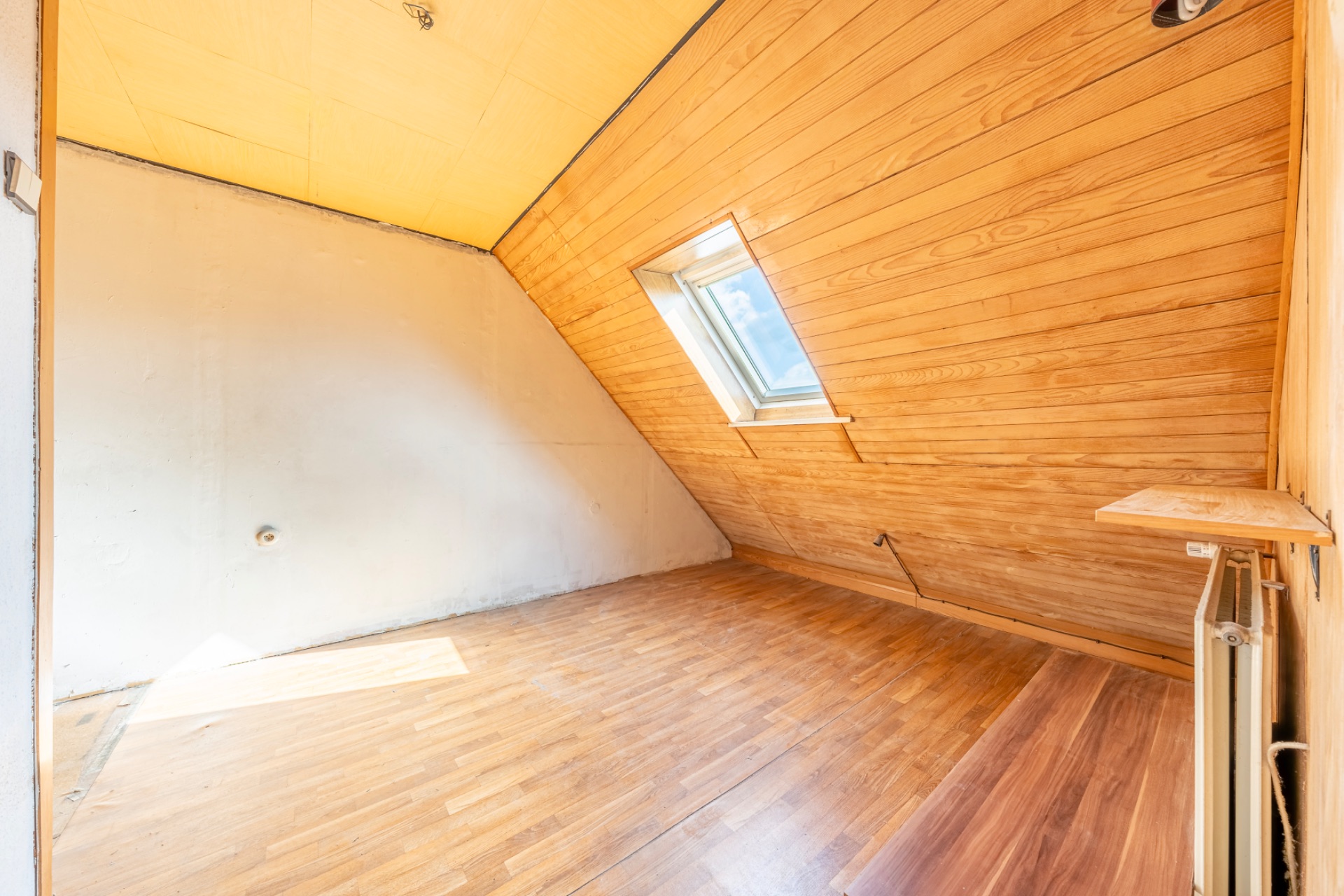 Helles Zimmer mit Holzboden, Dachschräge und Fenster in der Schräge.