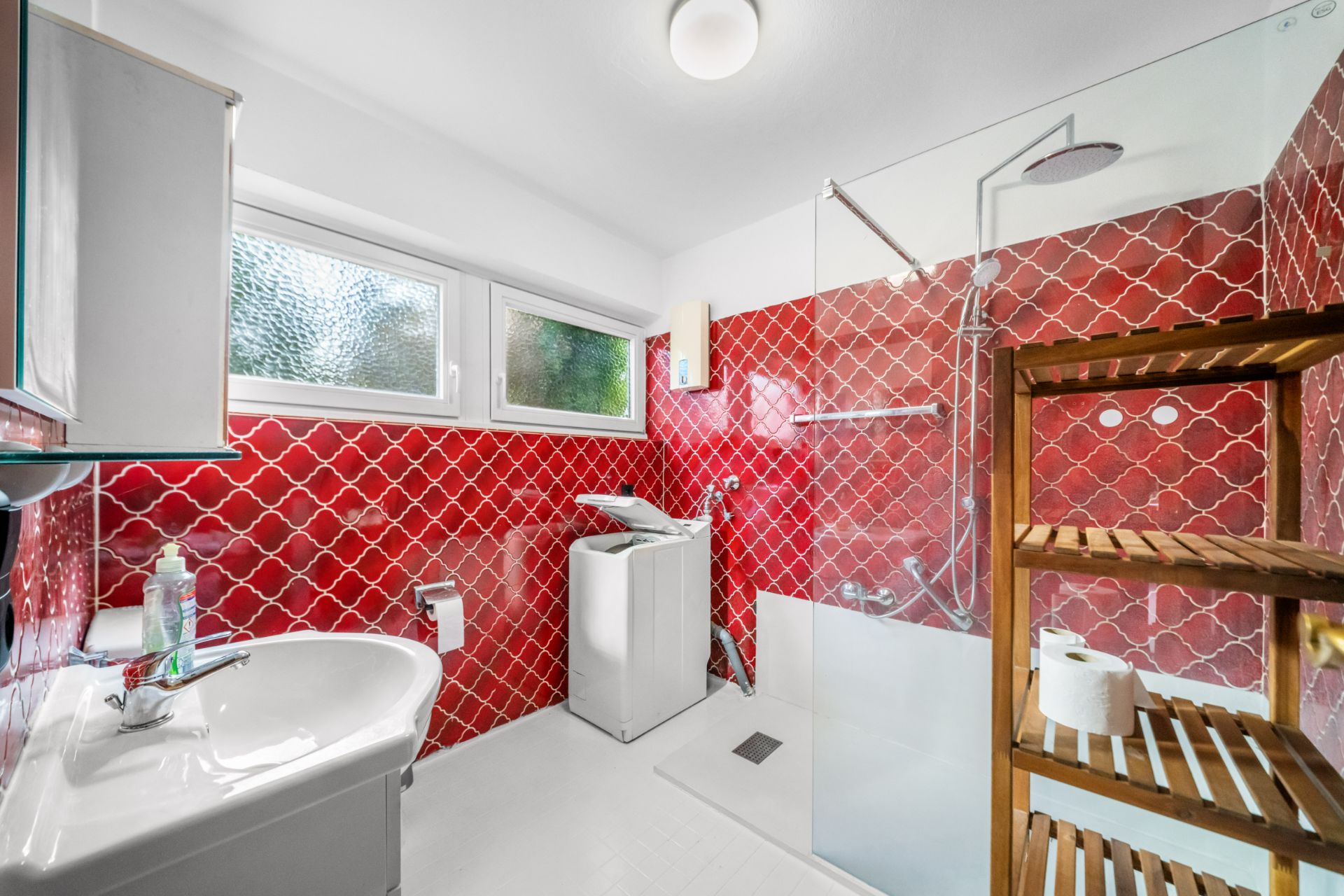 Modernes Badezimmer mit roter Fliesenwand, Waschmaschine, Dusche und Holzregal.