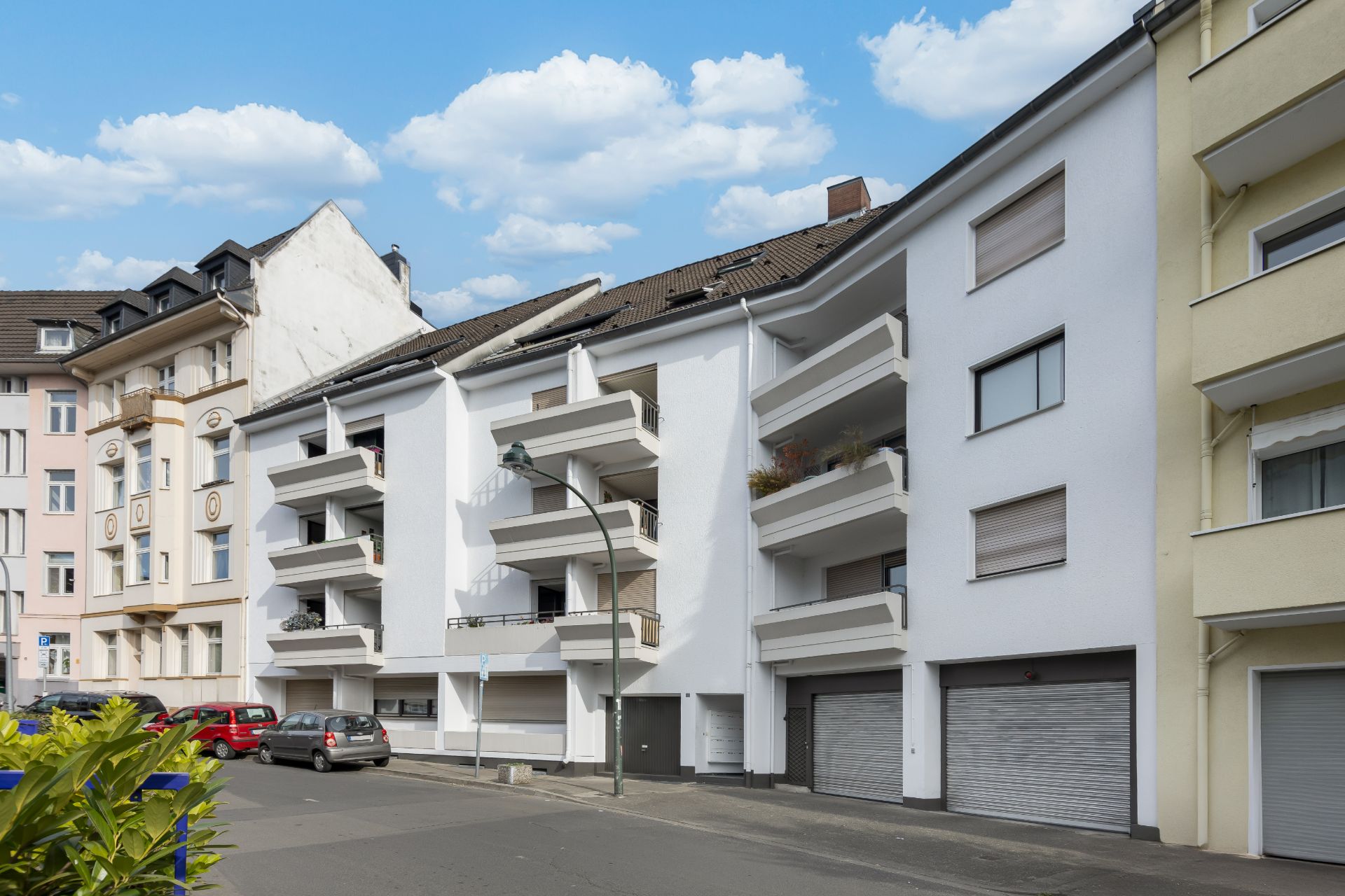 Mehrfamilienhaus mit weißen Balkonen und Garagen an einer ruhigen Straße.